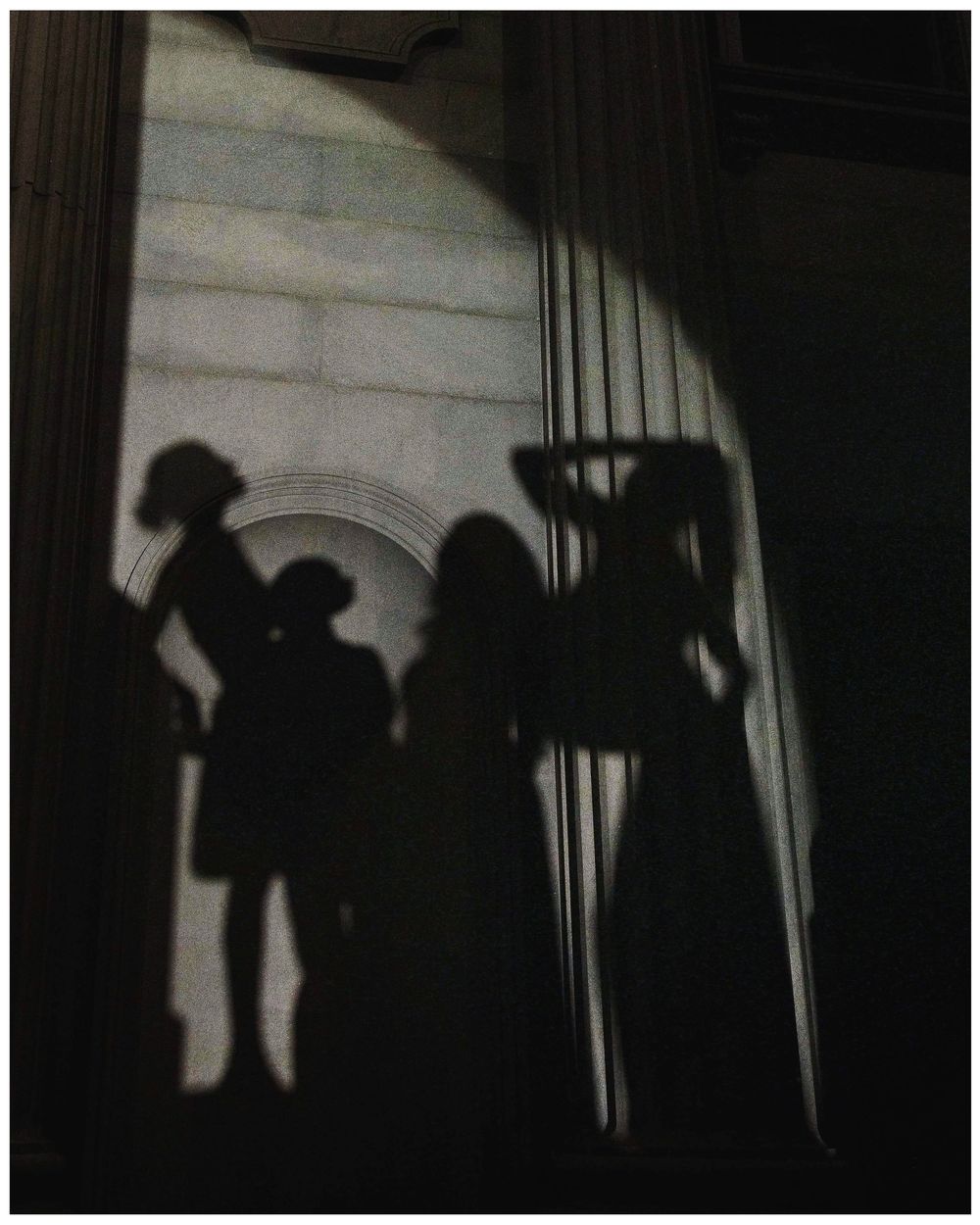 Dramatic shadow silhouettes of figures cast on a light wall with an arched architectural detail.