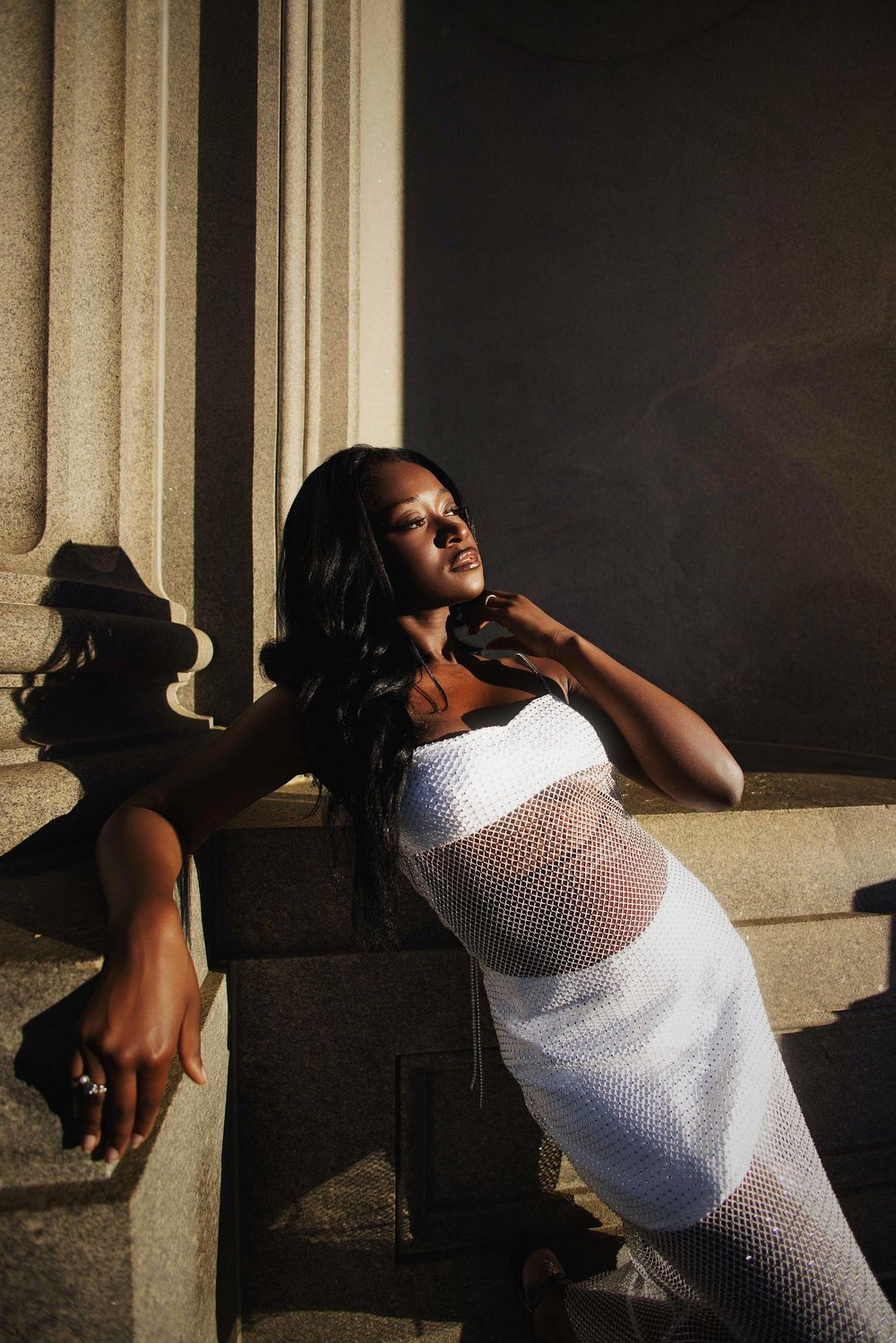 Person in white mesh top poses dramatically against architectural columns in dramatic lighting sequence.