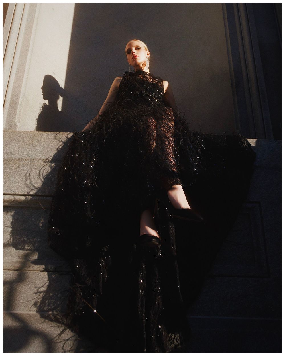 A person wearing an elegant black sparkly evening gown poses dramatically against a light colored wall in various stances.