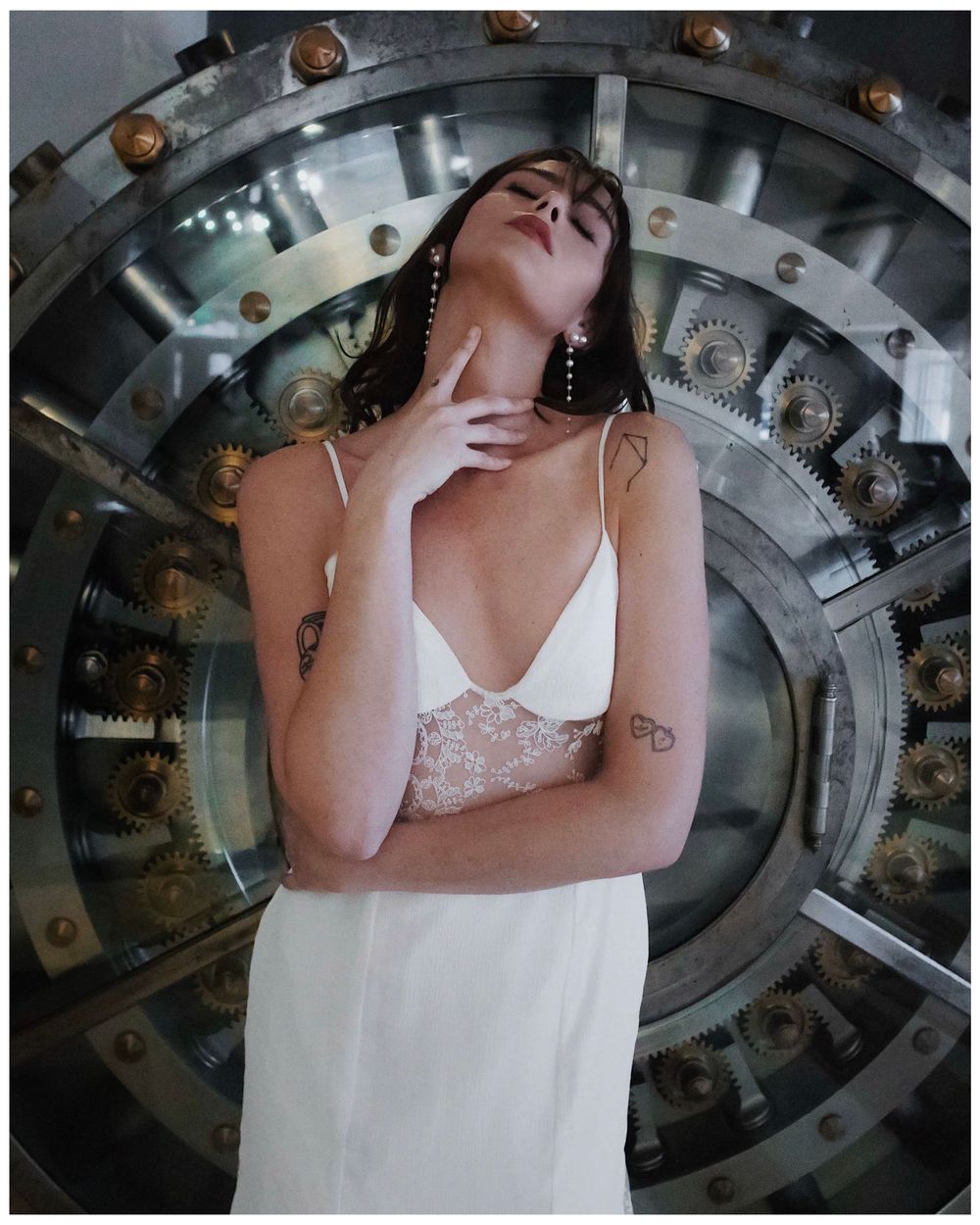 Artistic macro photo composition of someone in white dress viewed through circular geometric metal machinery pattern.