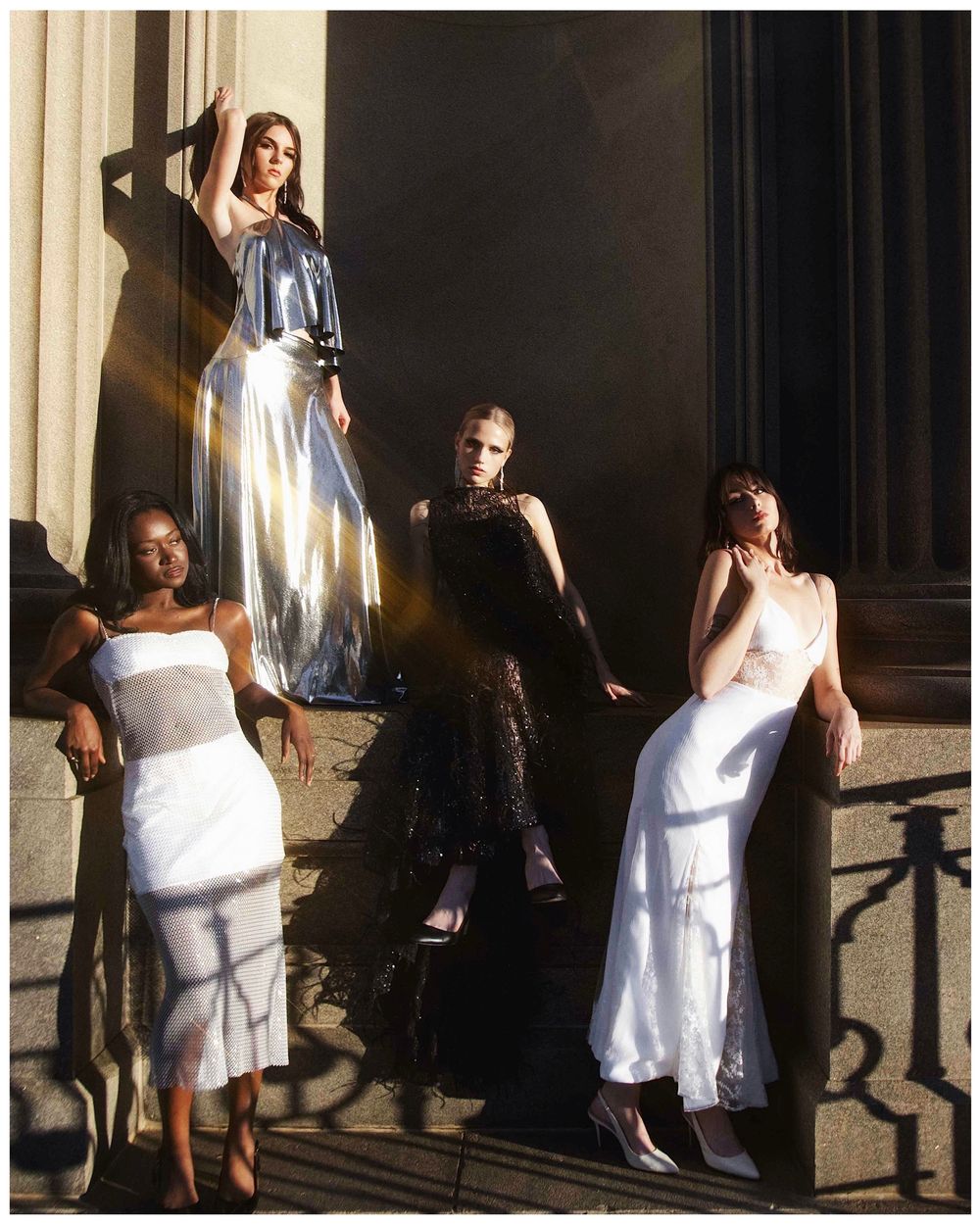 People in white dresses sitting in dramatic sunlight and shadows against a dark wall.