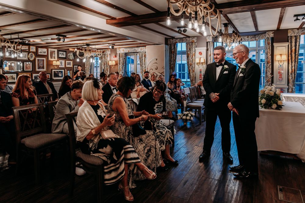 Panoramic view of people gathered in a rustic indoor venue with wooden beams and decorative lighting during an event.