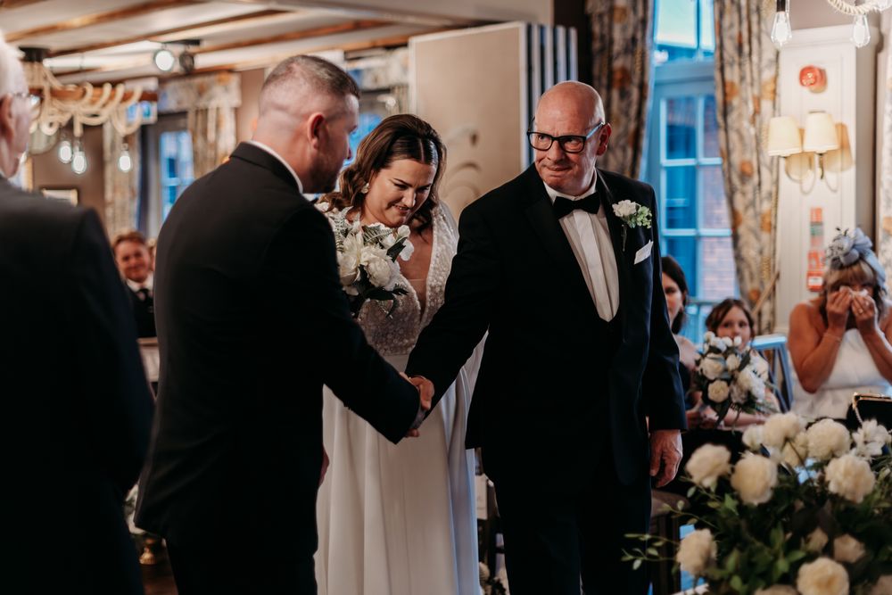 Wedding party reacts emotionally during ceremony at an elegant indoor venue with white floral decorations.