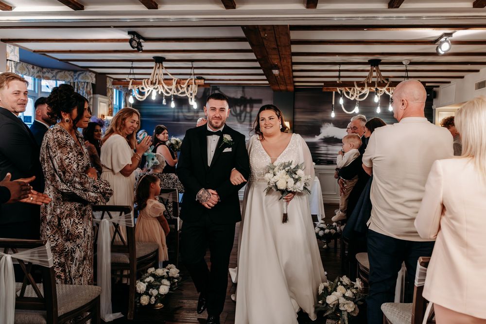 Wedding guests standing together and conversing at an elegant indoor reception venue with wooden beams.