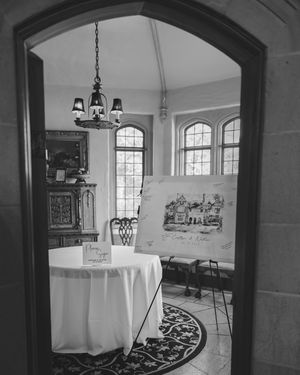 Black and white interior photograph showing multiple round dining tables with white tablecloths and elegant hanging chandeliers.