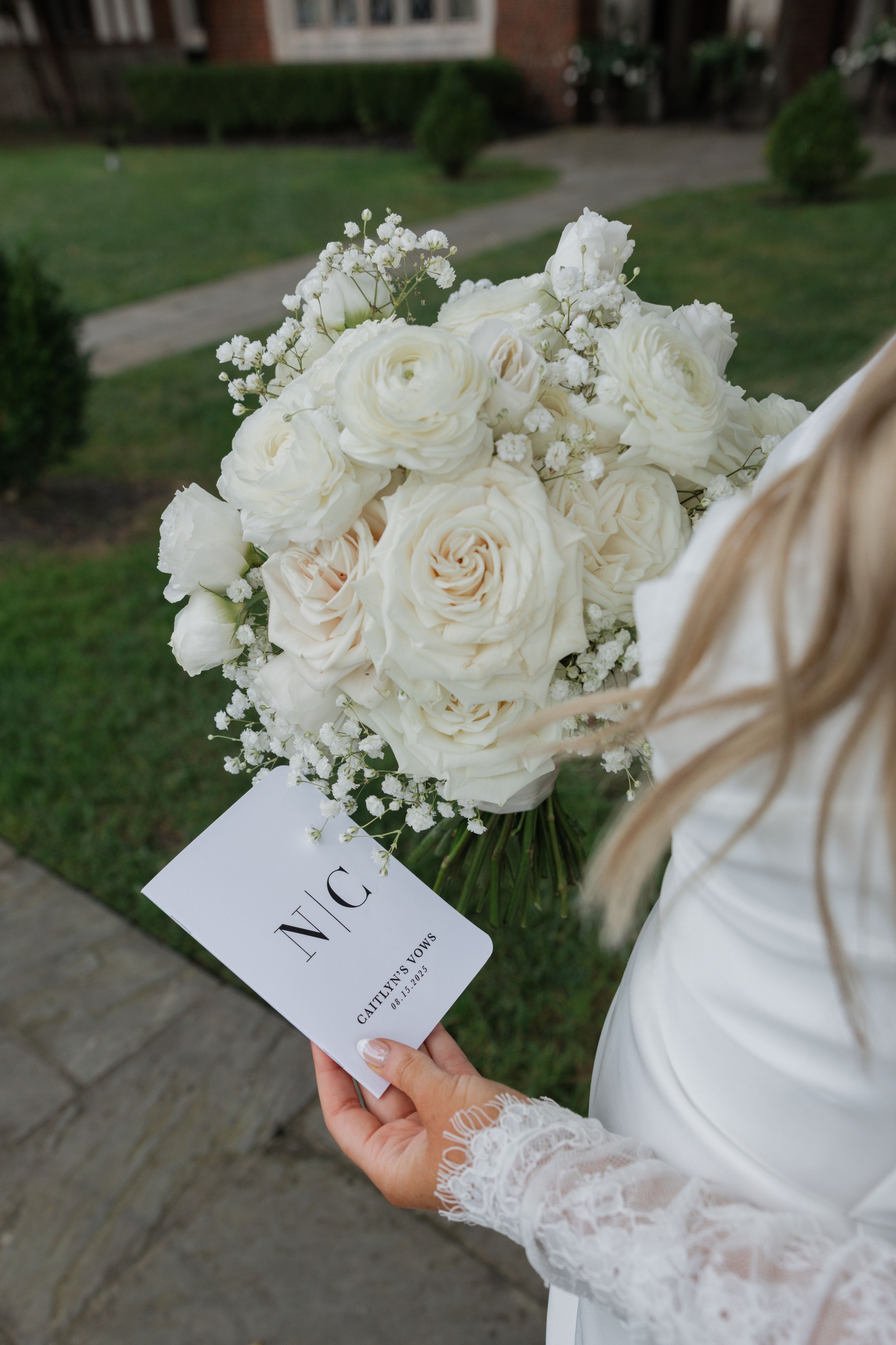 Elegant white rose and baby's breath wedding bouquet held alongside a monogrammed card on stone steps.