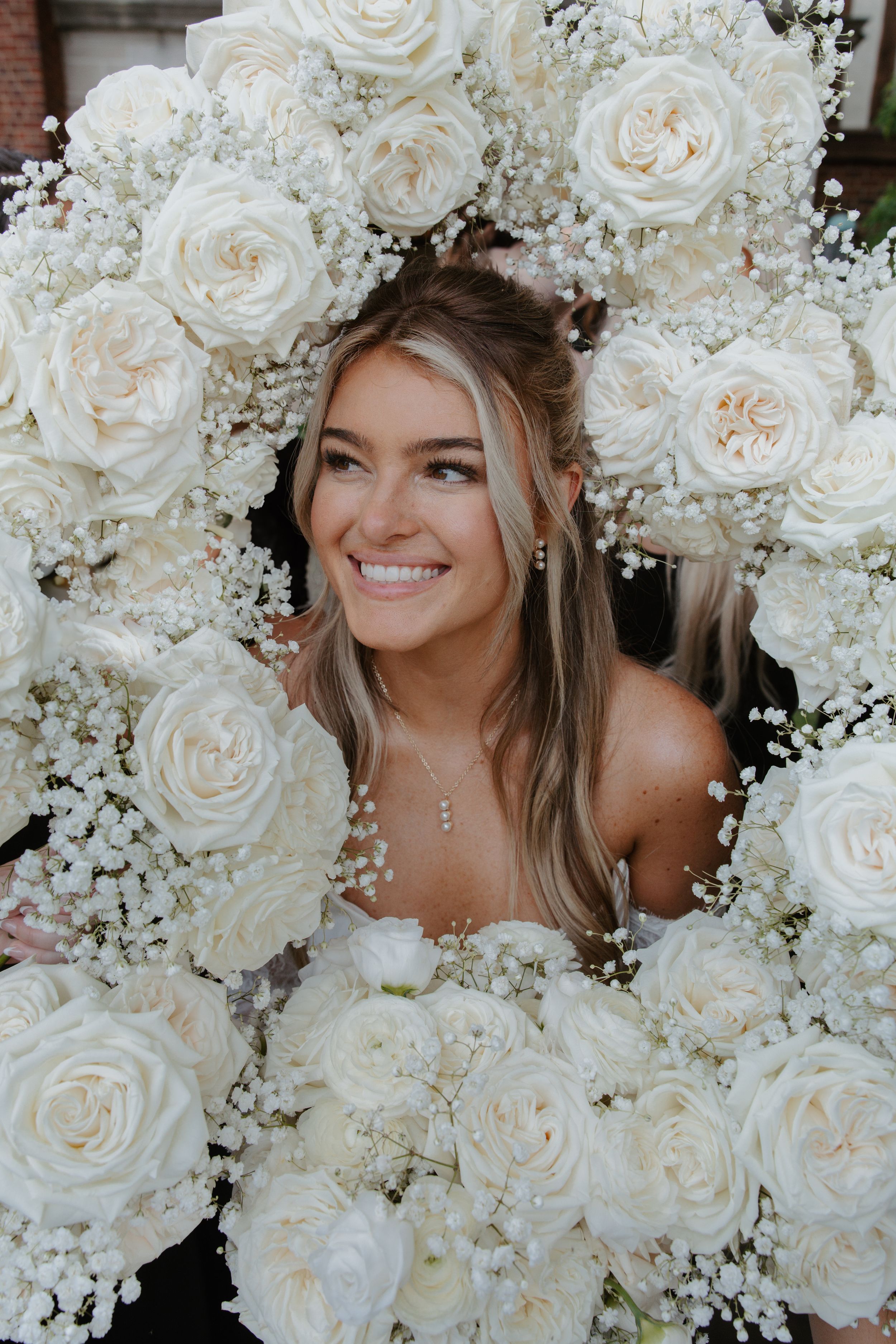 Beautiful bridal portrait surrounded by lush white roses and baby's breath flowers in a romantic garden setting.