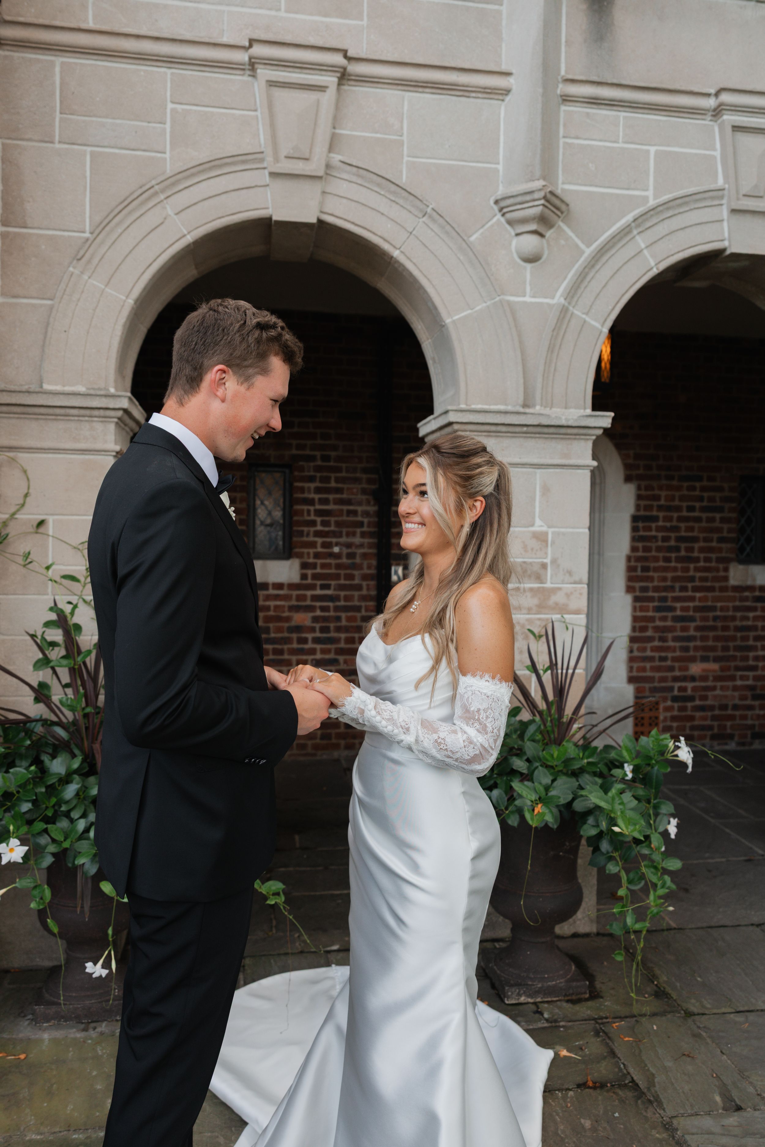 A couple in formal wedding attire share a romantic dance moment under a stone archway.