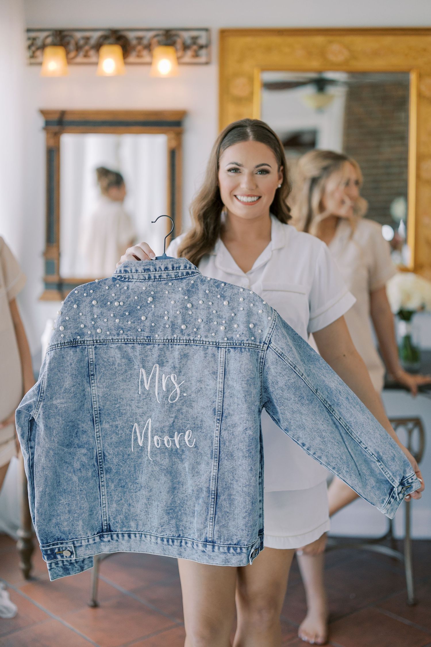 Custom denim jacket with "Mrs" embroidered text displayed on wooden hangers for a wedding event.