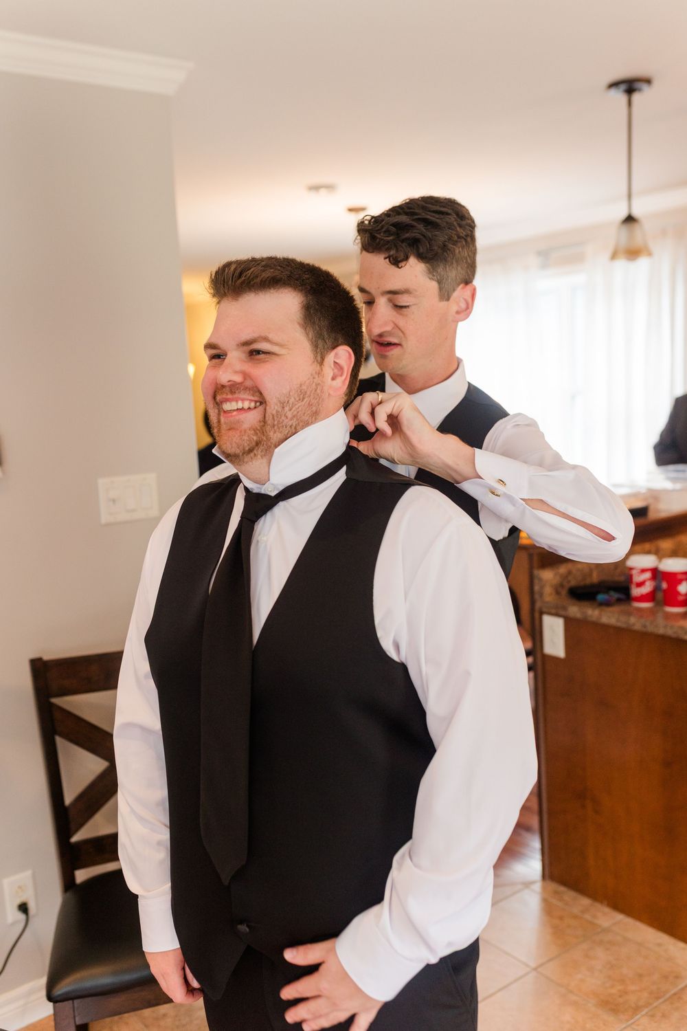 Two people share a lighthearted moment while getting dressed in formal attire before a special event.