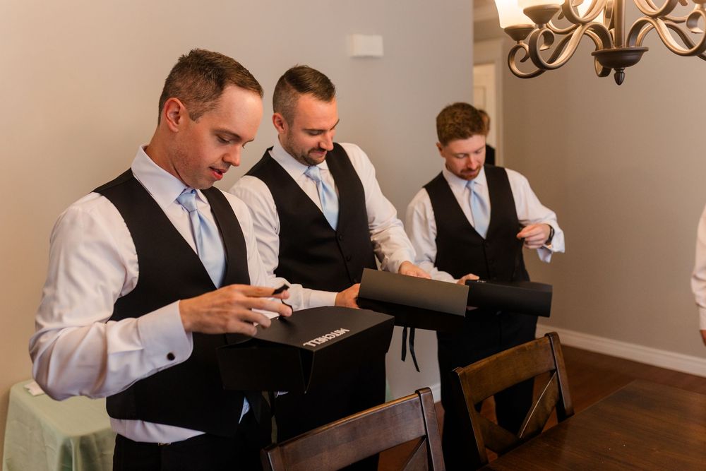 Group of men in formal attire reading letters while sitting at a wooden table under a chandelier.