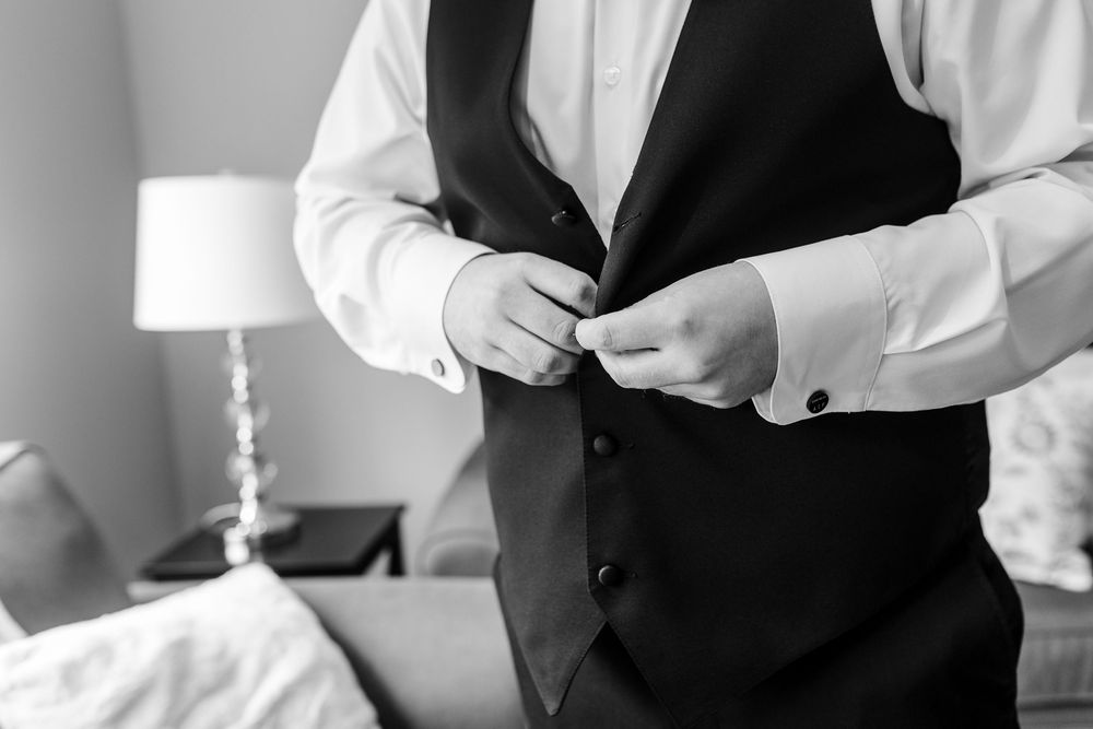Groomsmen help with wedding day preparations in a light-filled room.