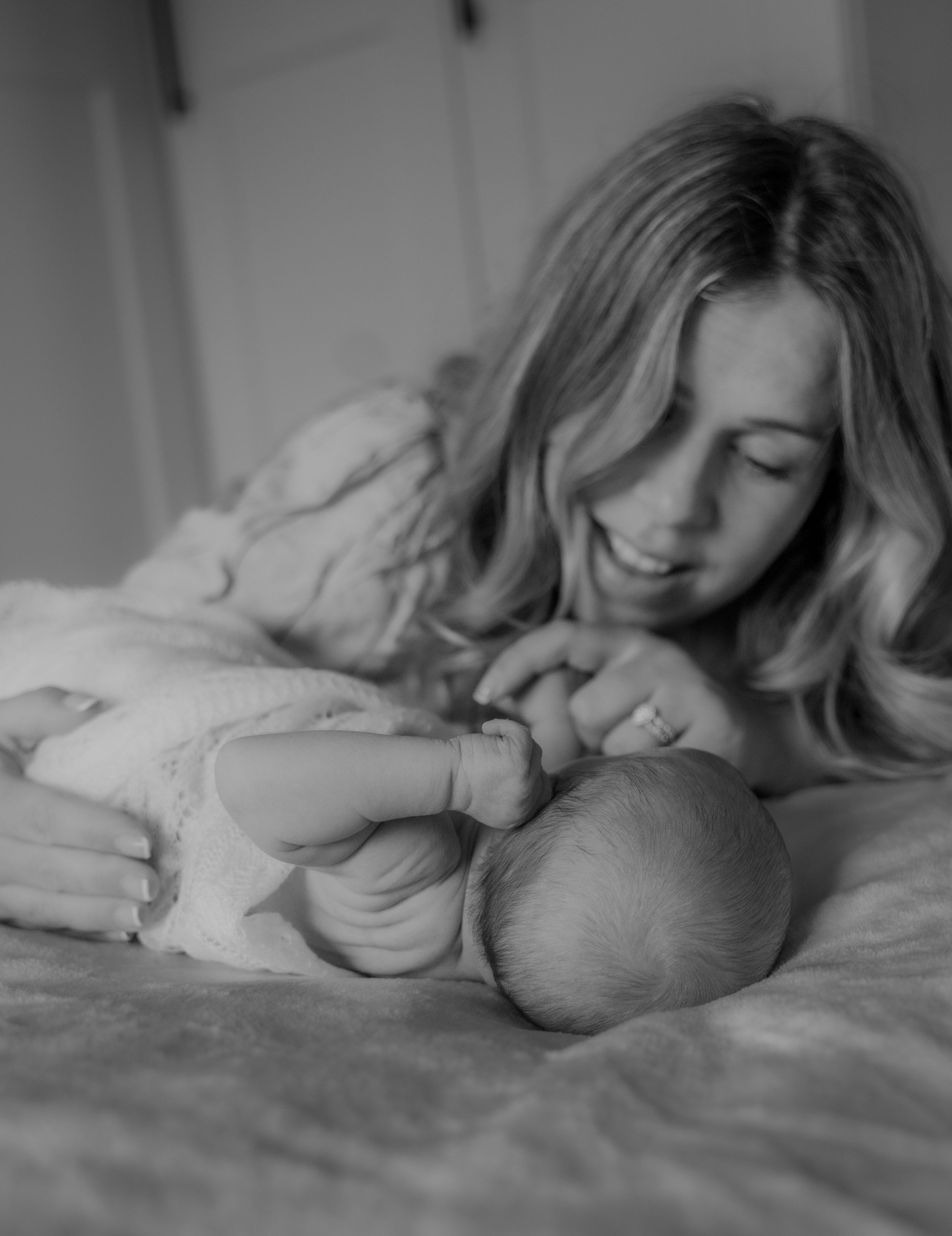 A tender black and white photo series showing a parent snuggling with their sleeping baby on a bed.