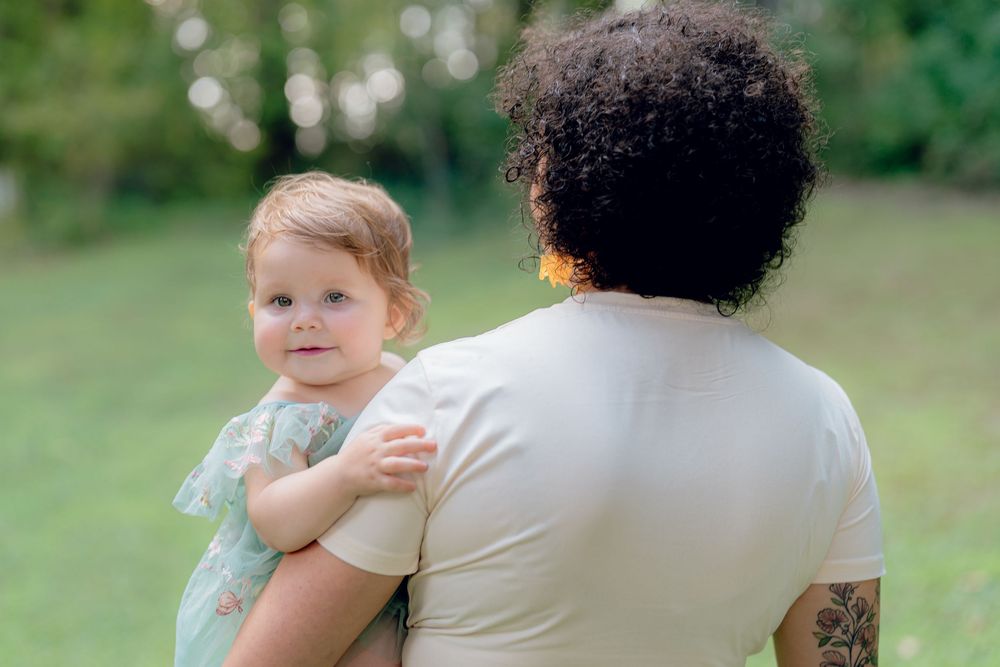 A tender outdoor moment captured in a park setting with green trees in the background at One Year Milestone session in Akron, Ohio