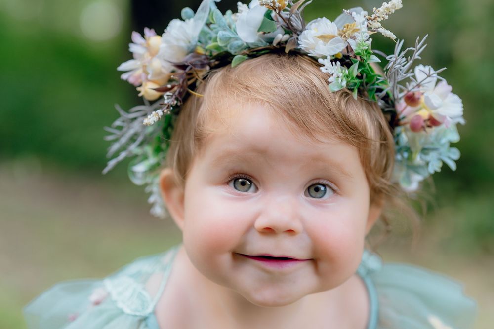 A close up portrait showing bright eyes and a floral crown against a soft green outdoor background in Akron, OH for One Year Photo Session