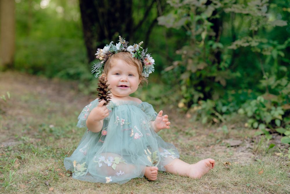 A small child in a mint dress sits on grass wearing a delicate floral crown in a garden setting in Akron, Ohio for a One Year Milestone Pic