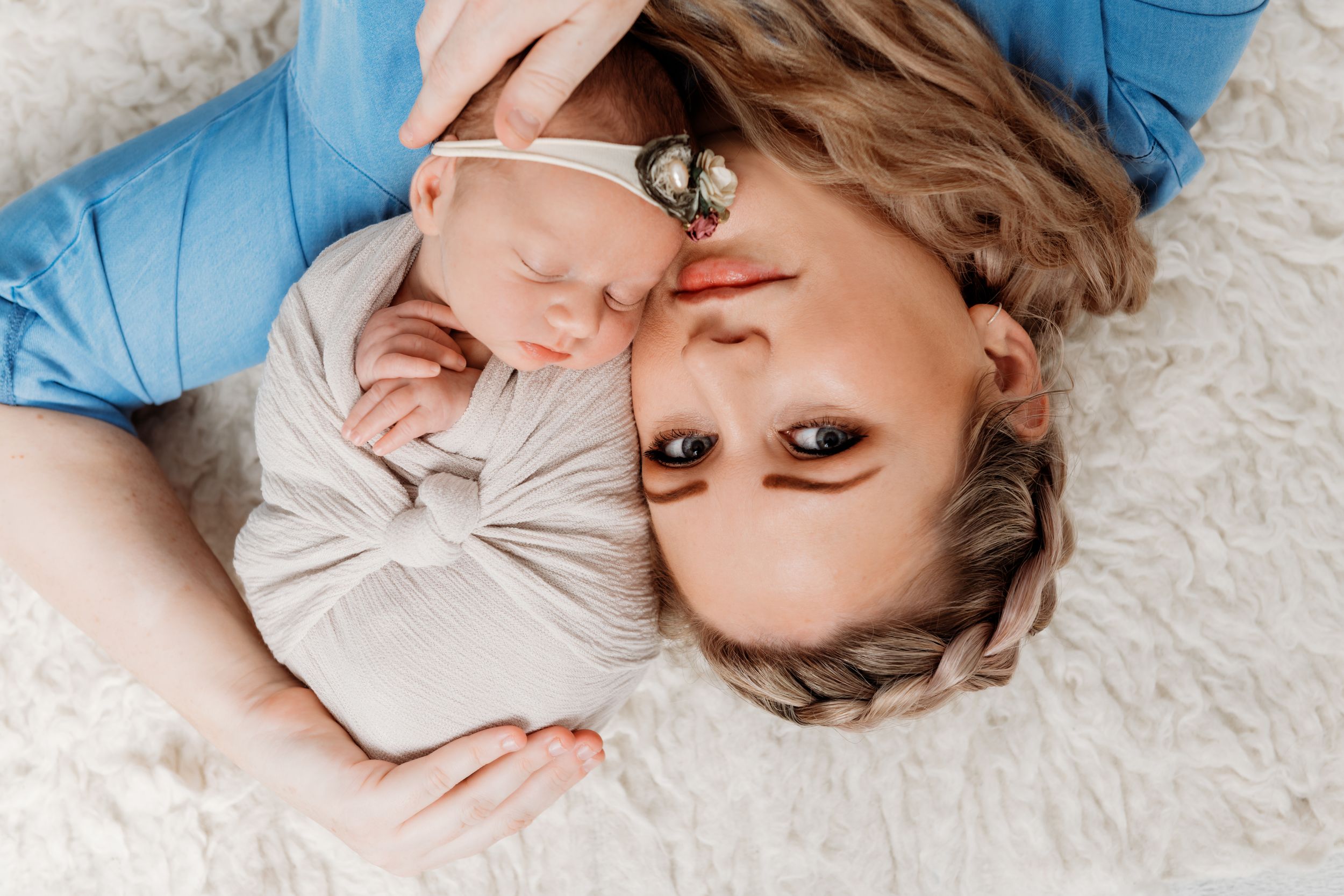 Overhead portrait of parent and sleeping newborn on soft white surface.