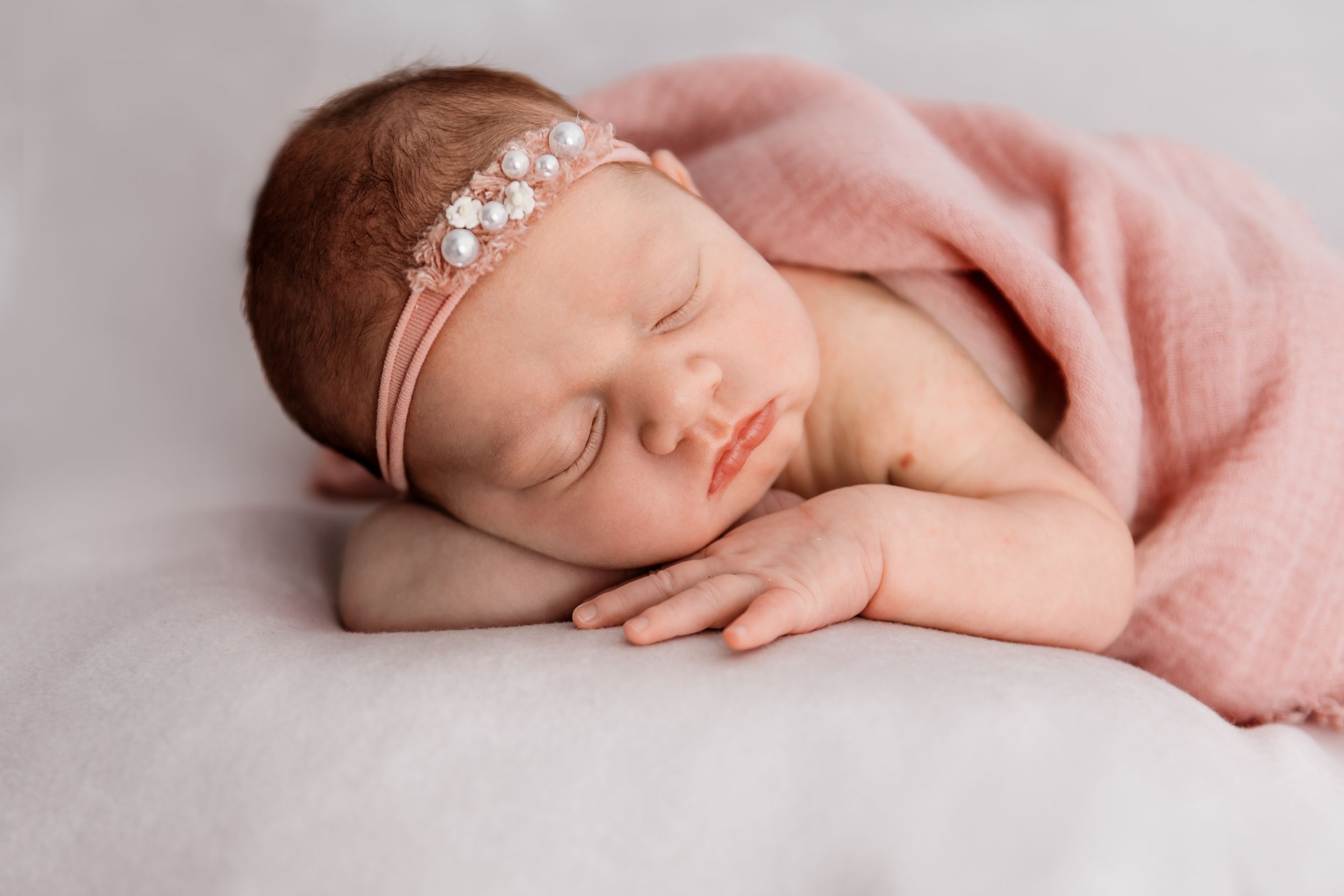 Sleeping newborn wrapped in pink blanket wearing delicate floral headband.