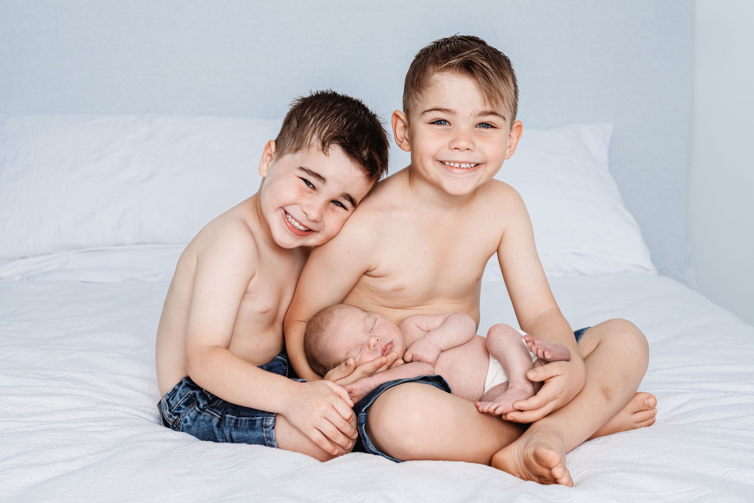 Two young boys laughing and playing together on white bedding.