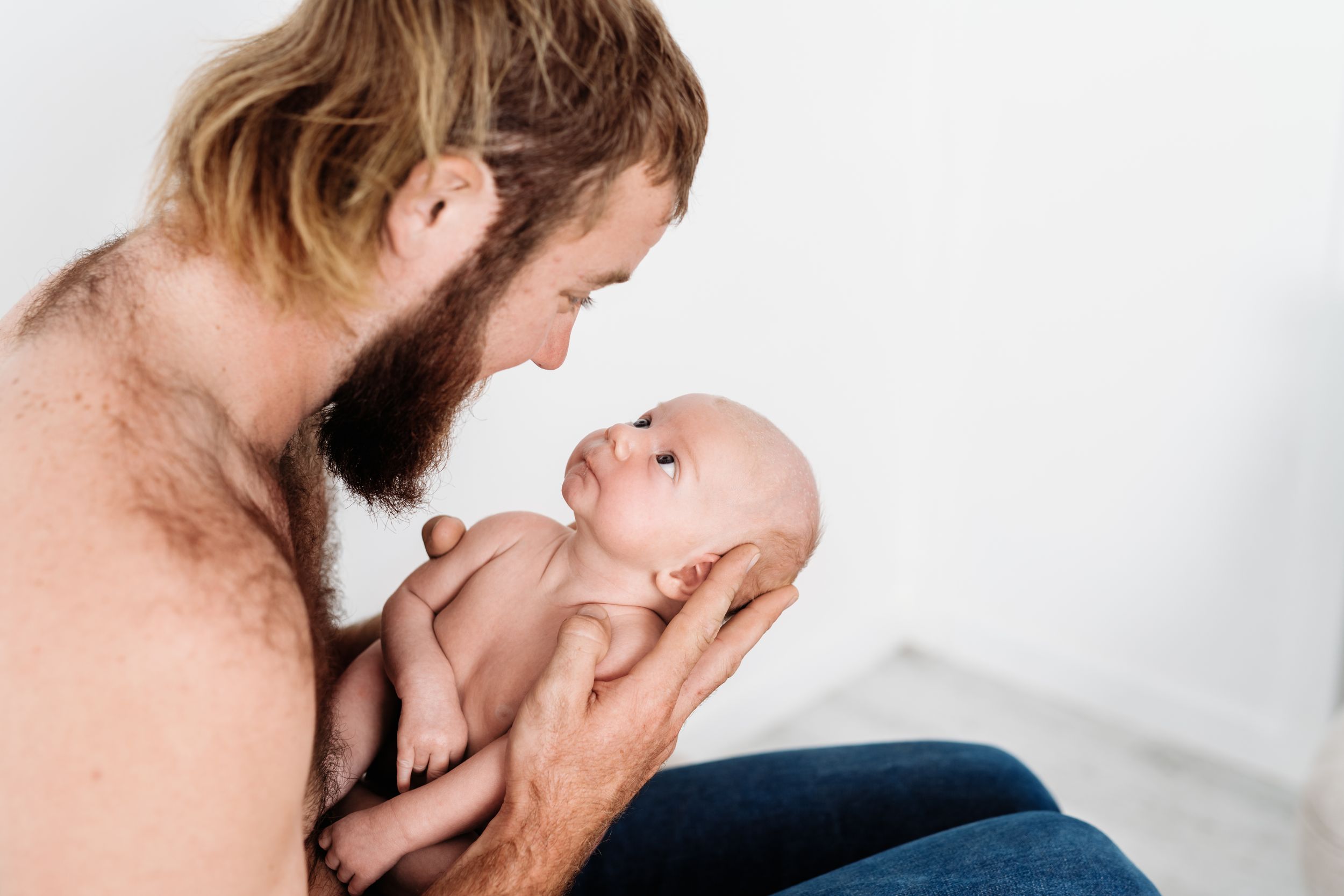 A tender moment between a bearded parent and their baby against white background.