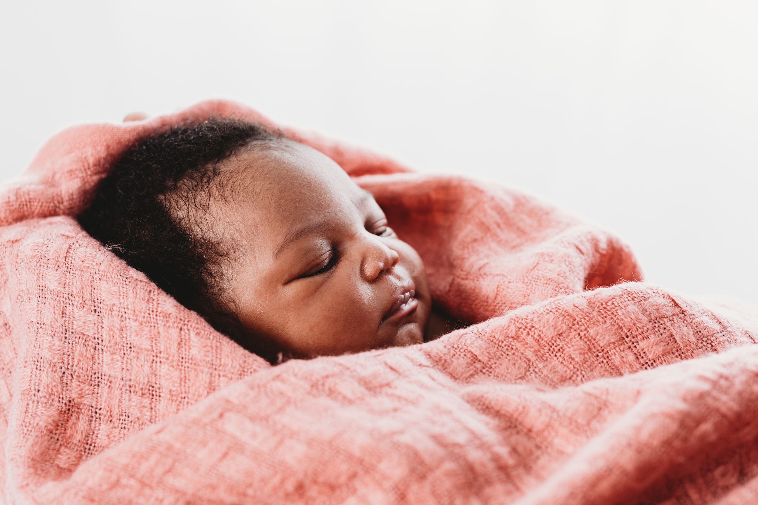 A peaceful sleeping baby wrapped in coral pink blanket against white background.
