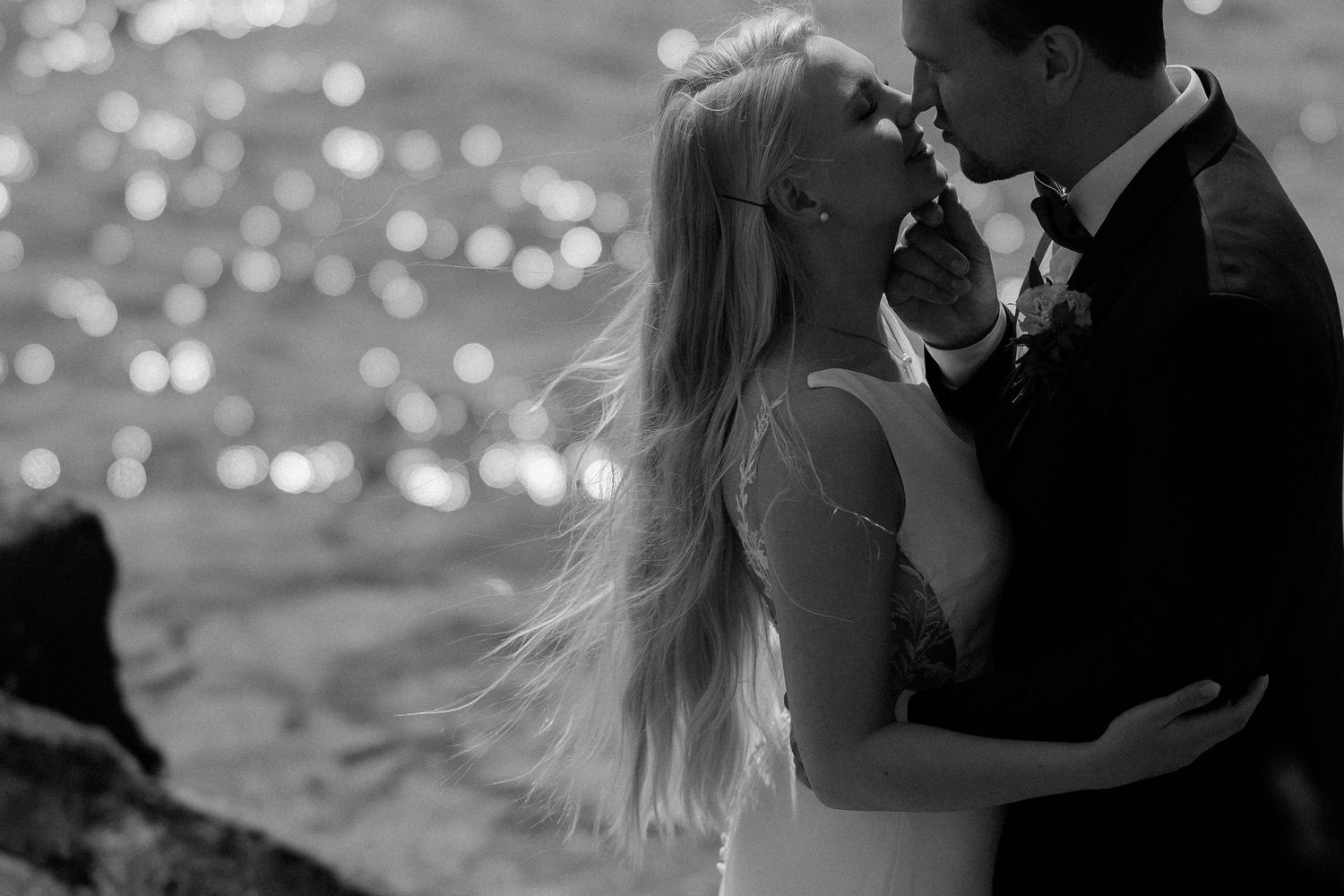 A couple in formal attire shares an intimate dance together at a celebration with lights twinkling in the background.