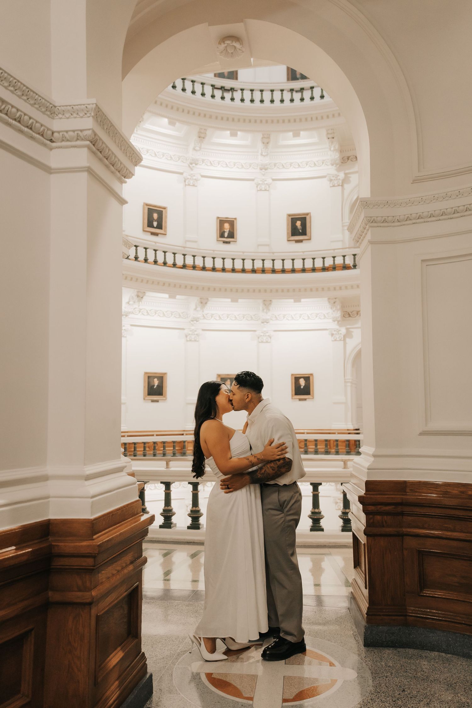 A couple in white and beige outfits share a romantic moment on a vintage wooden staircase.