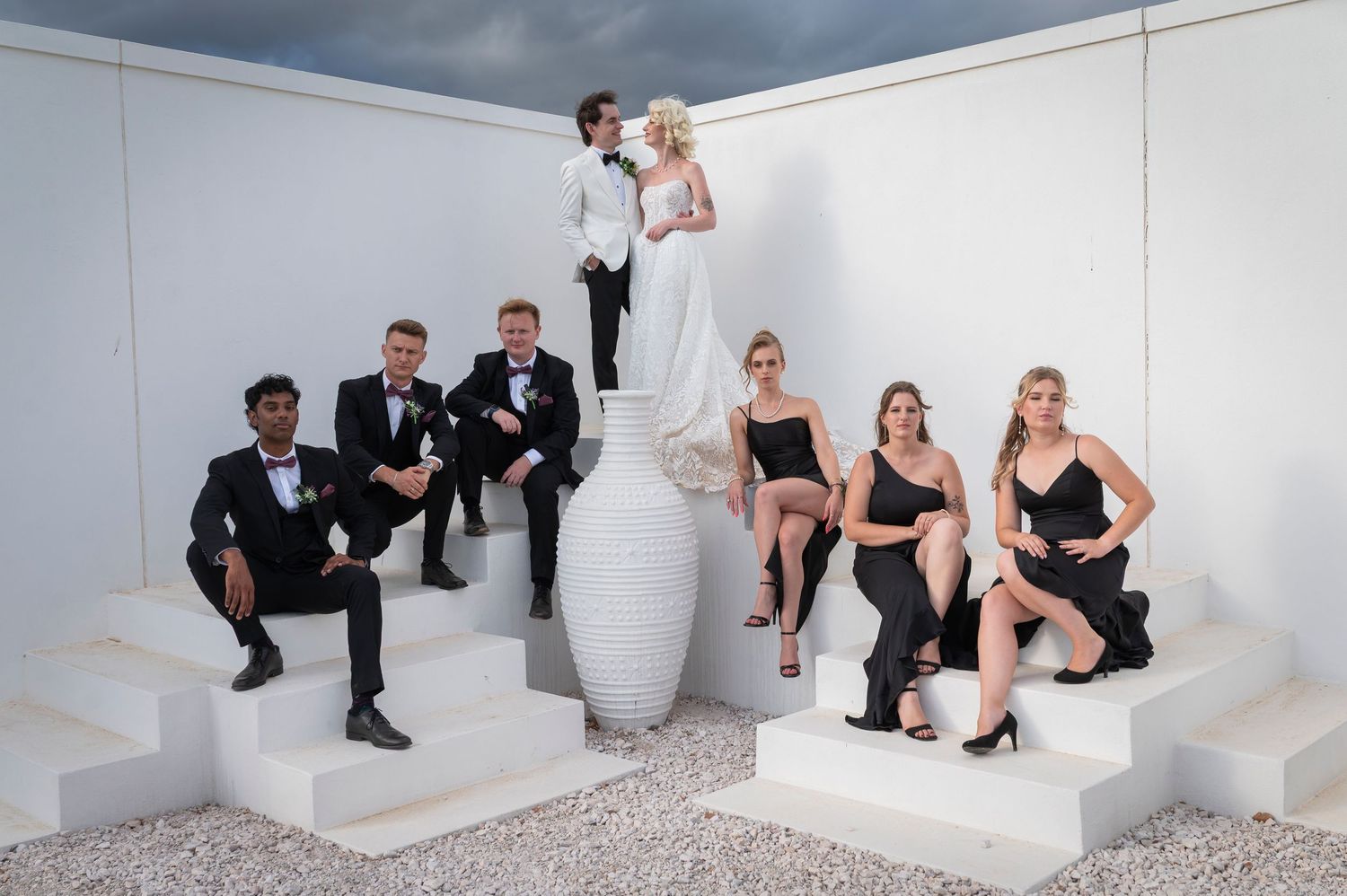 Wedding party poses creatively on white modern staircase in stylish black and white formal attire.