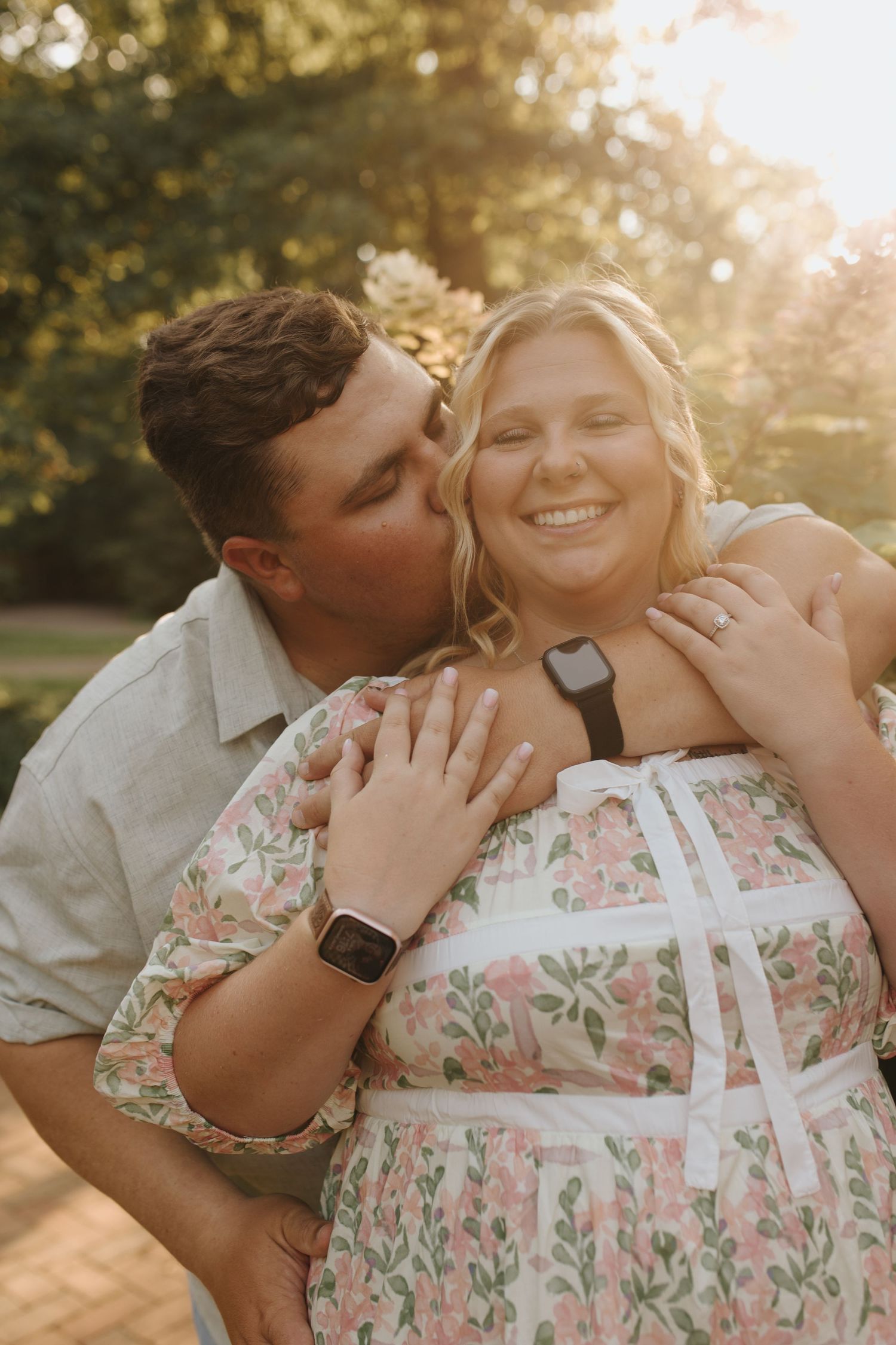 Newly engaged couple in a close embrace where future groom is kissing future bride's cheek.