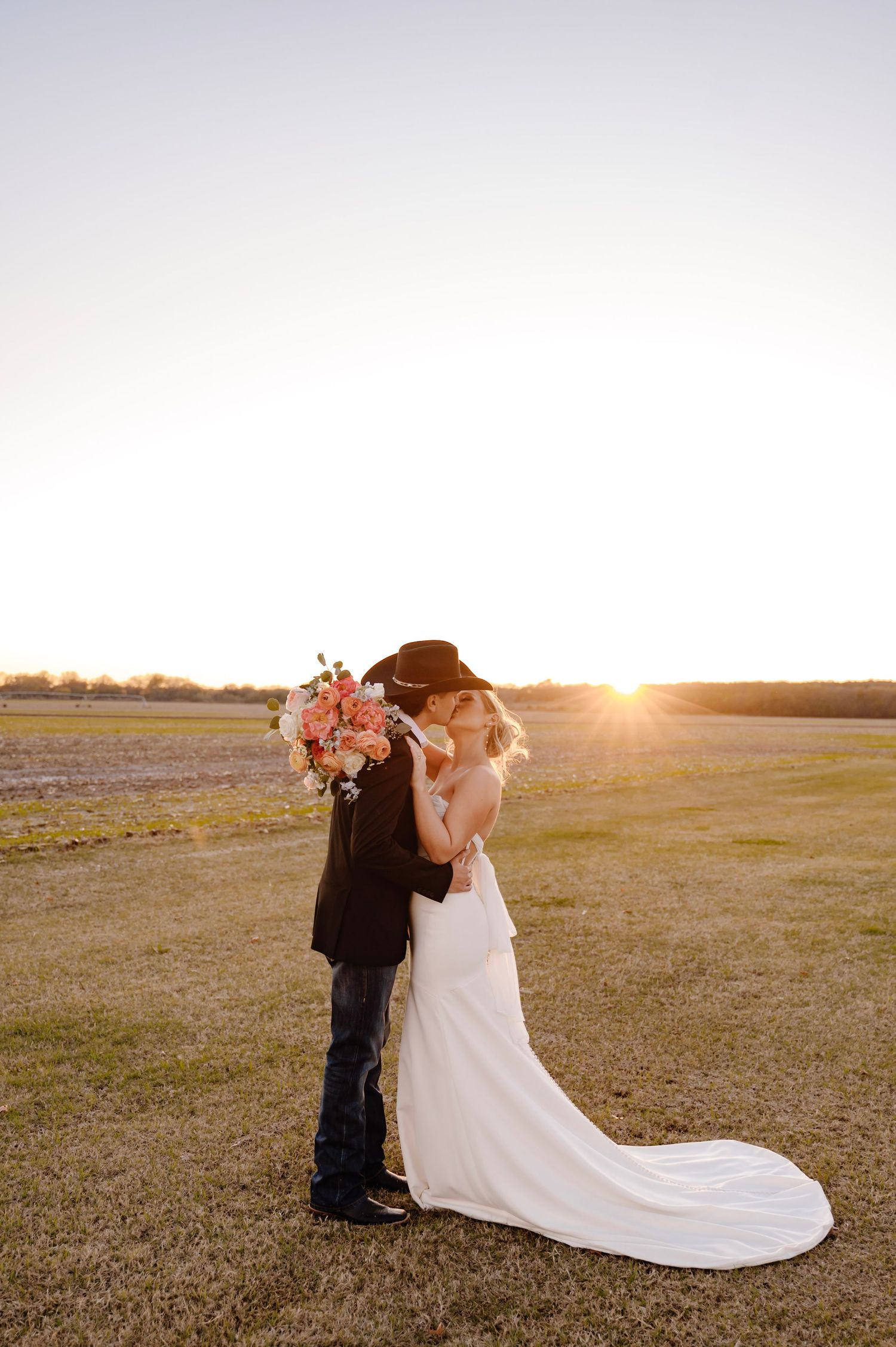 A couple shares an embrace in a golden sunlit field during their sunset wedding photo session.