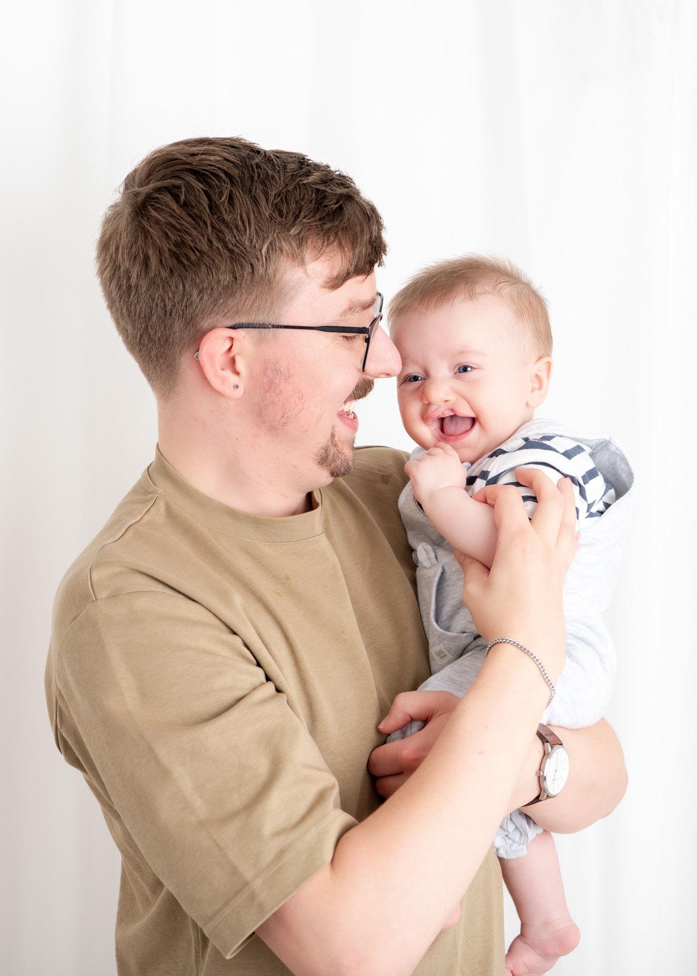 Candid moment of parent and laughing baby sharing a close moment against white background.