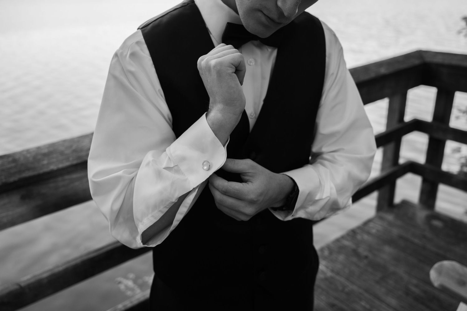 Groom adjusting their white dress shirt cuffs against a dark background.