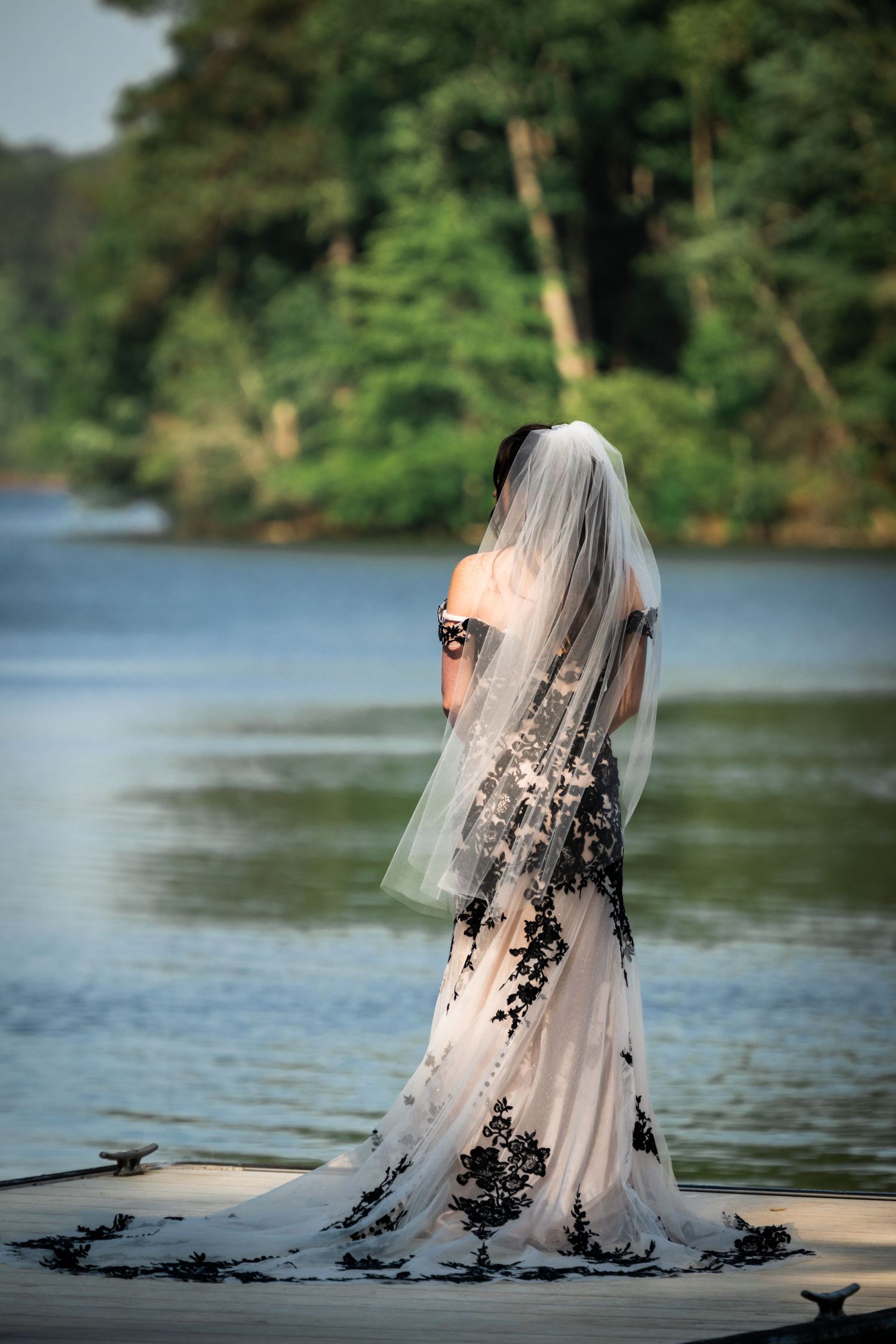 Wedding dress with black lace detailing photographed against a serene lakeside backdrop.