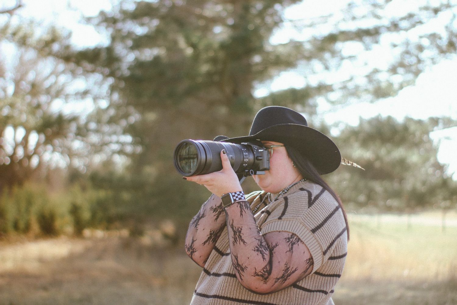 Photographer with camera in sunflower field wearing glasses and baseball cap.