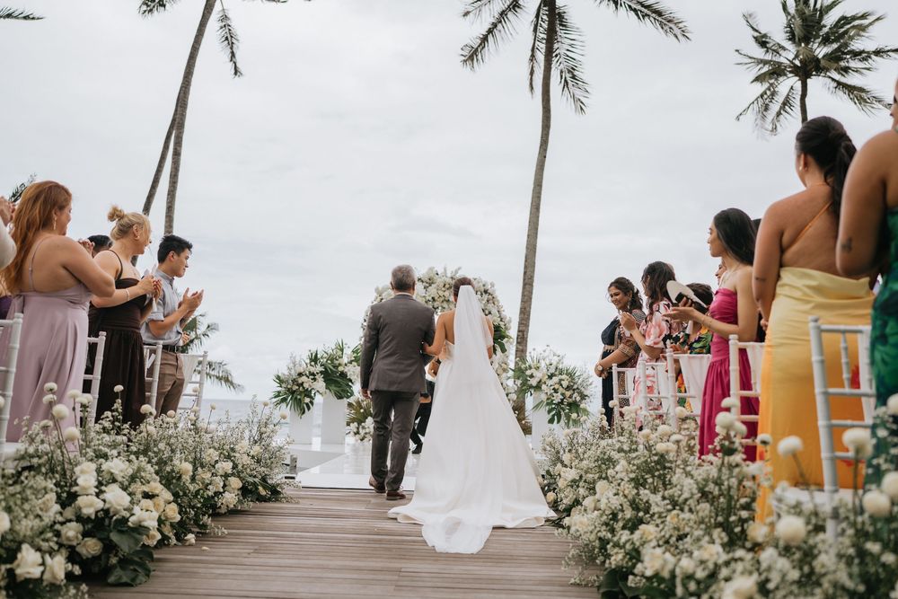Oceanfront wedding ceremony setup with white floral arrangements and palm trees.