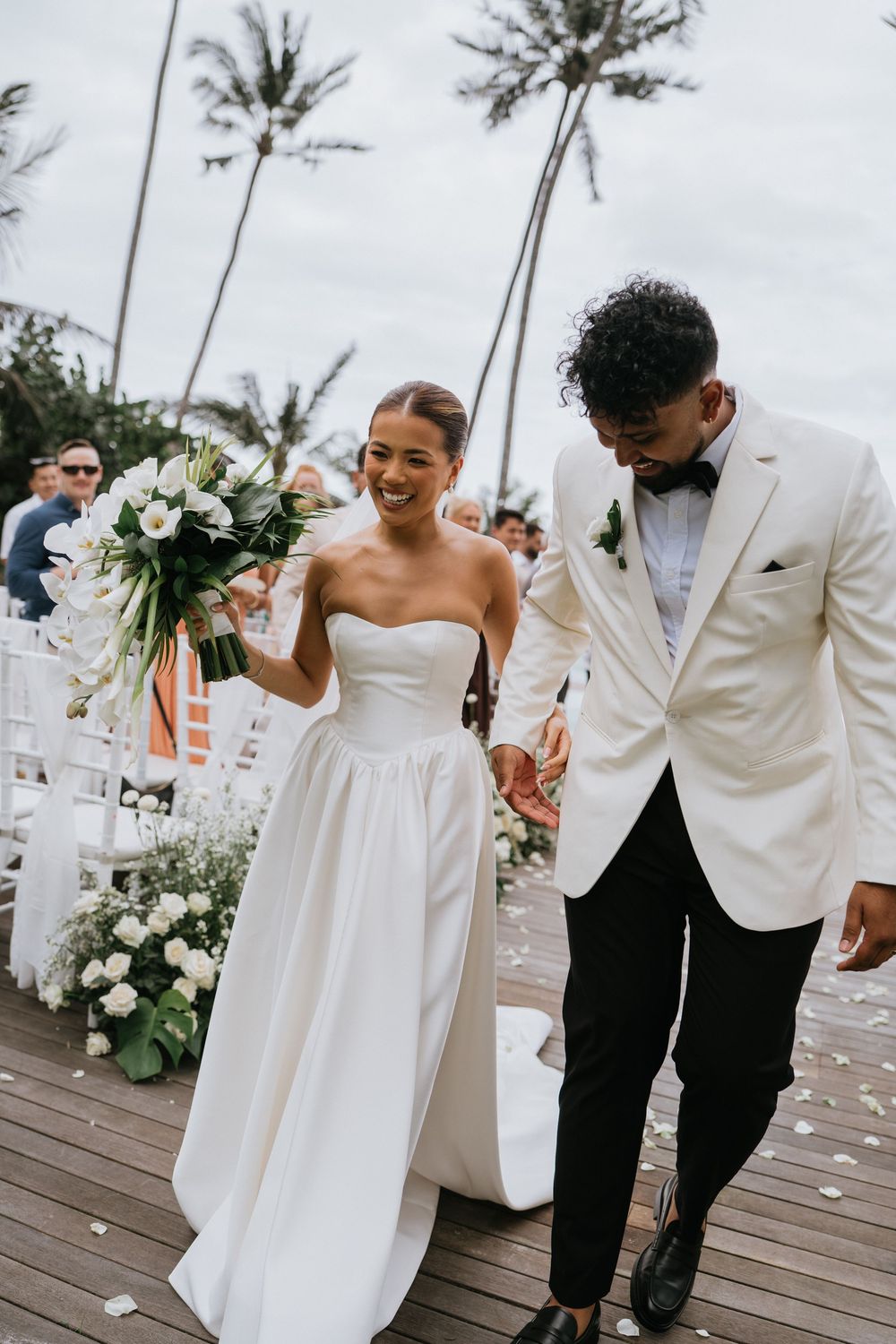 Newlyweds sharing joyful moments on wooden deck with white floral arrangements.