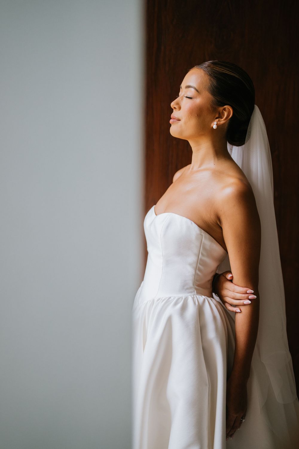 Side profile of bride in classic white strapless wedding gown with veil.