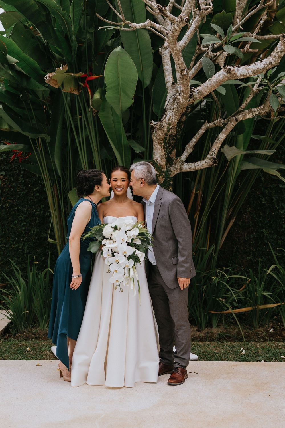 Wedding party poses against lush tropical garden backdrop.