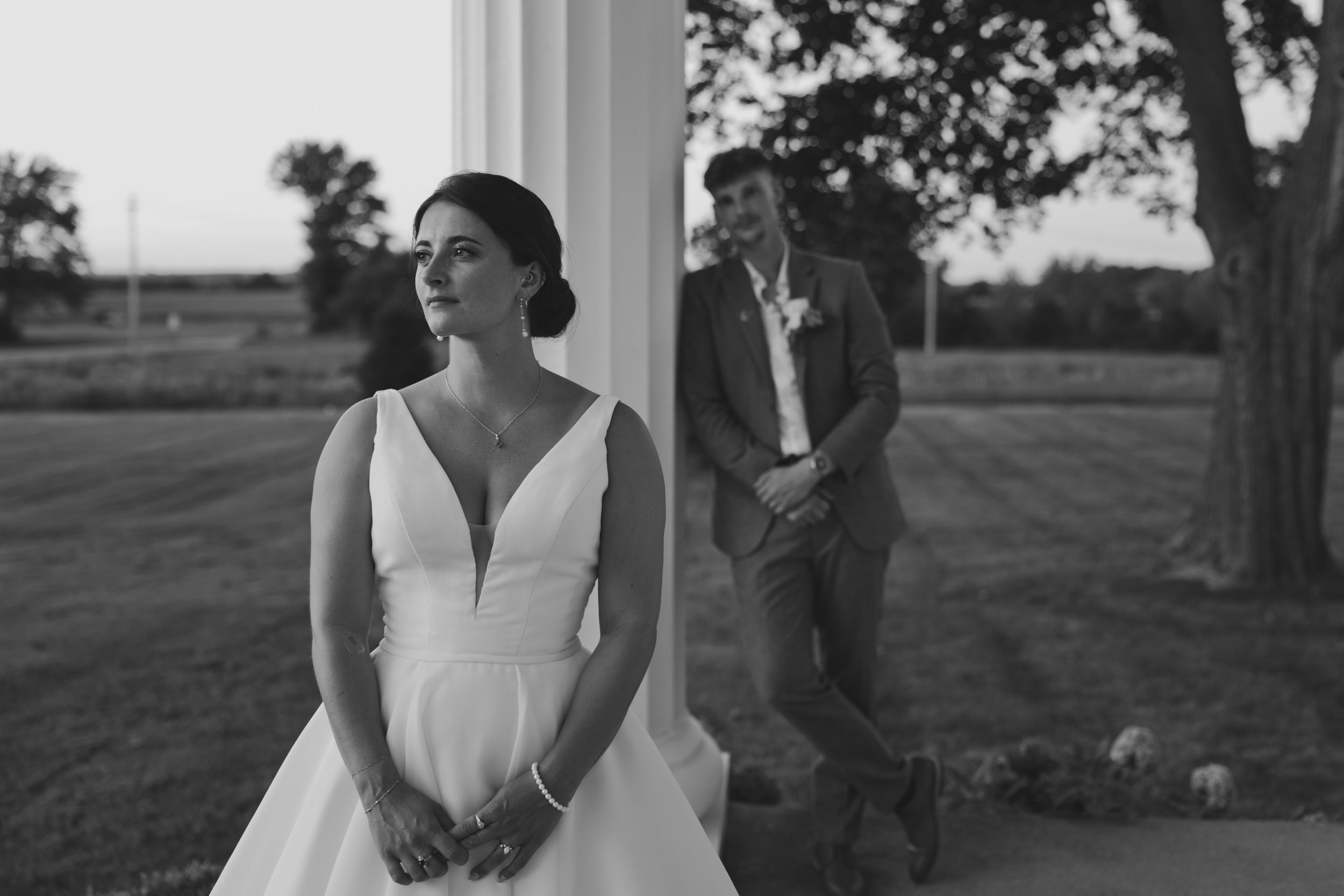 A person in an elegant white wedding dress stands in front of columns at an outdoor venue during golden hour.