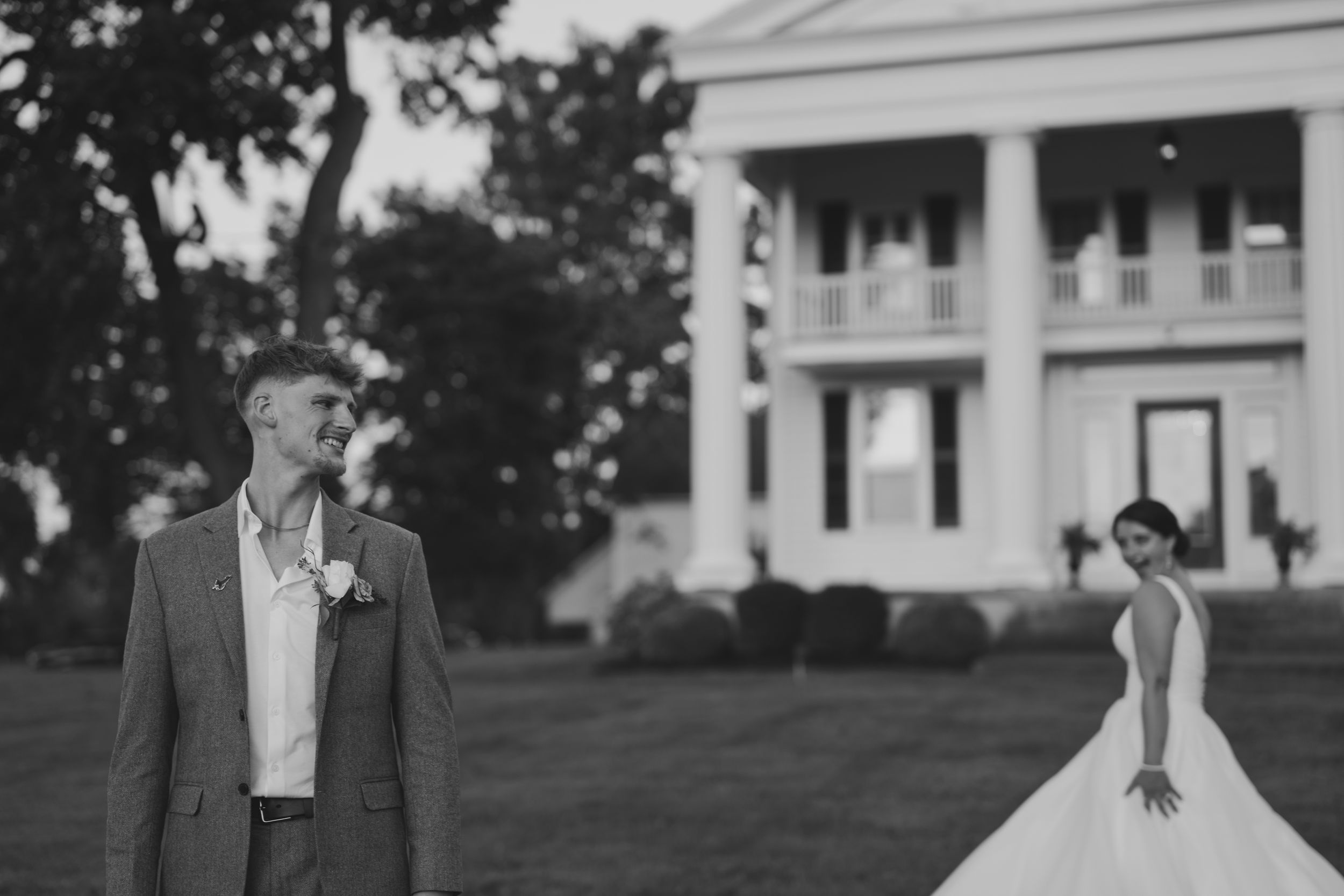 Black and white wedding photo of figures posing in front of a stately Southern mansion with white columns.