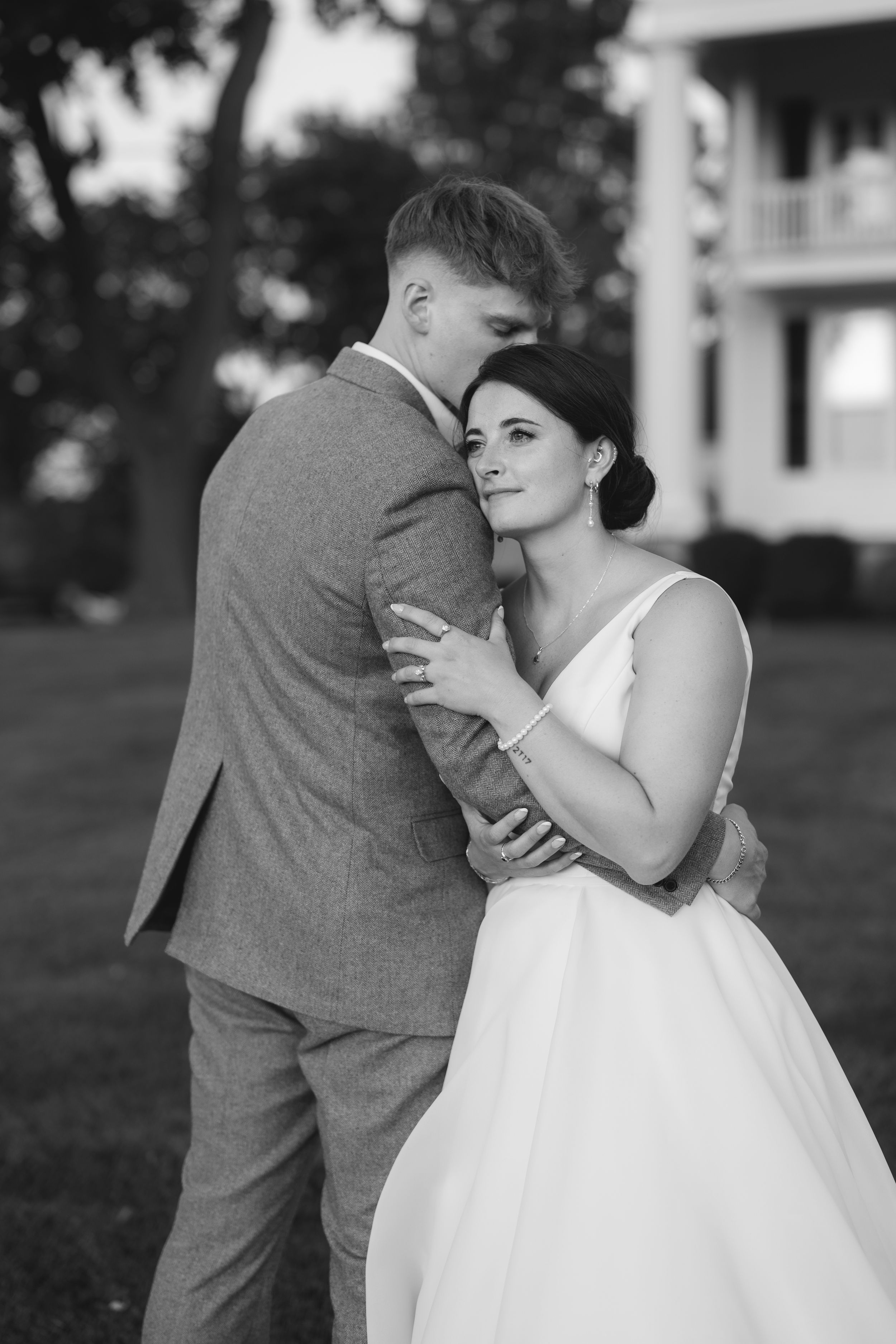 A wedding couple shares a playful moment in black and white as the bride taps the groom's shoulder from behind.