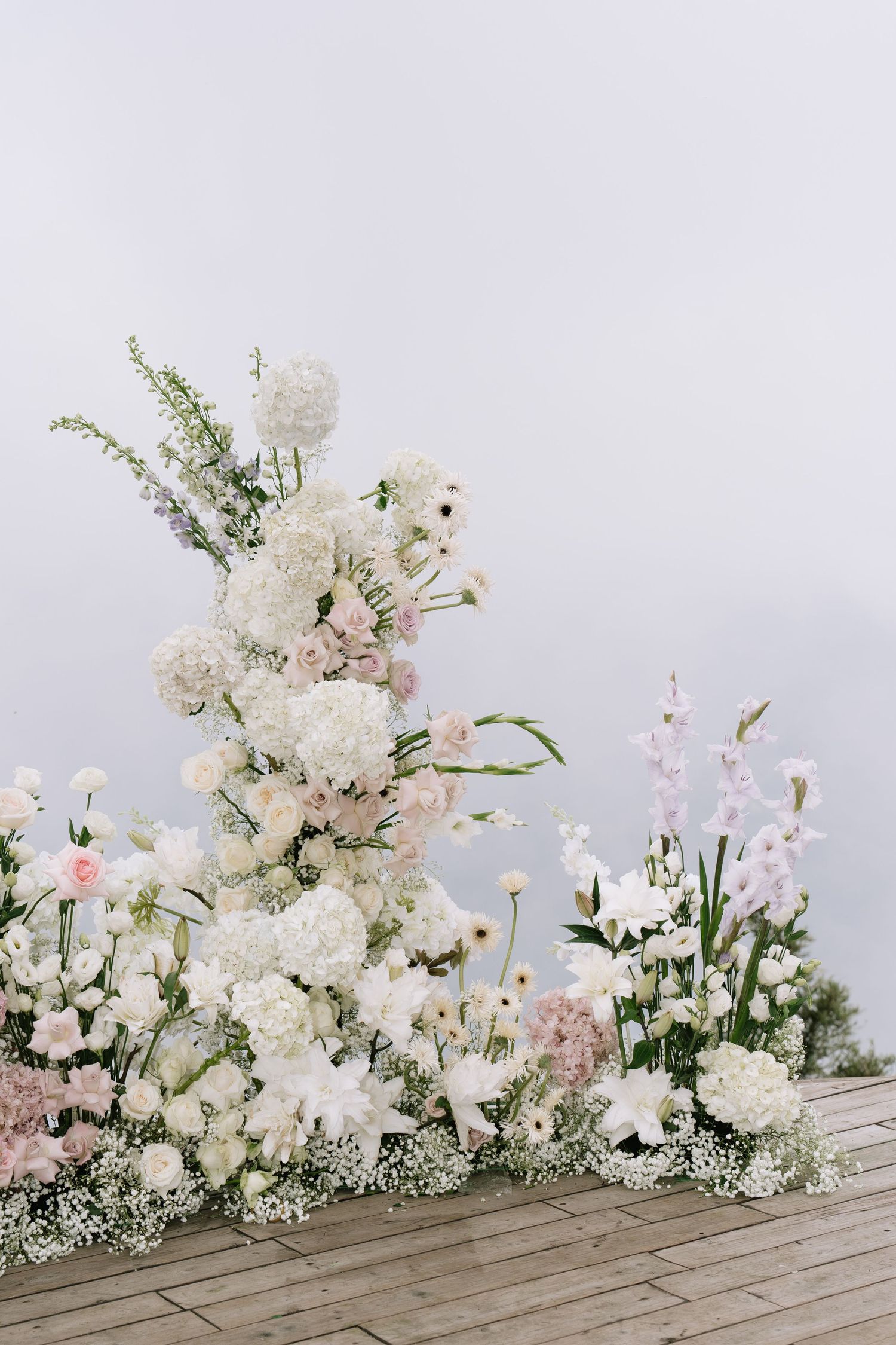 Elegant white and pink wedding flower arrangement with hydrangeas and roses on a wooden deck.