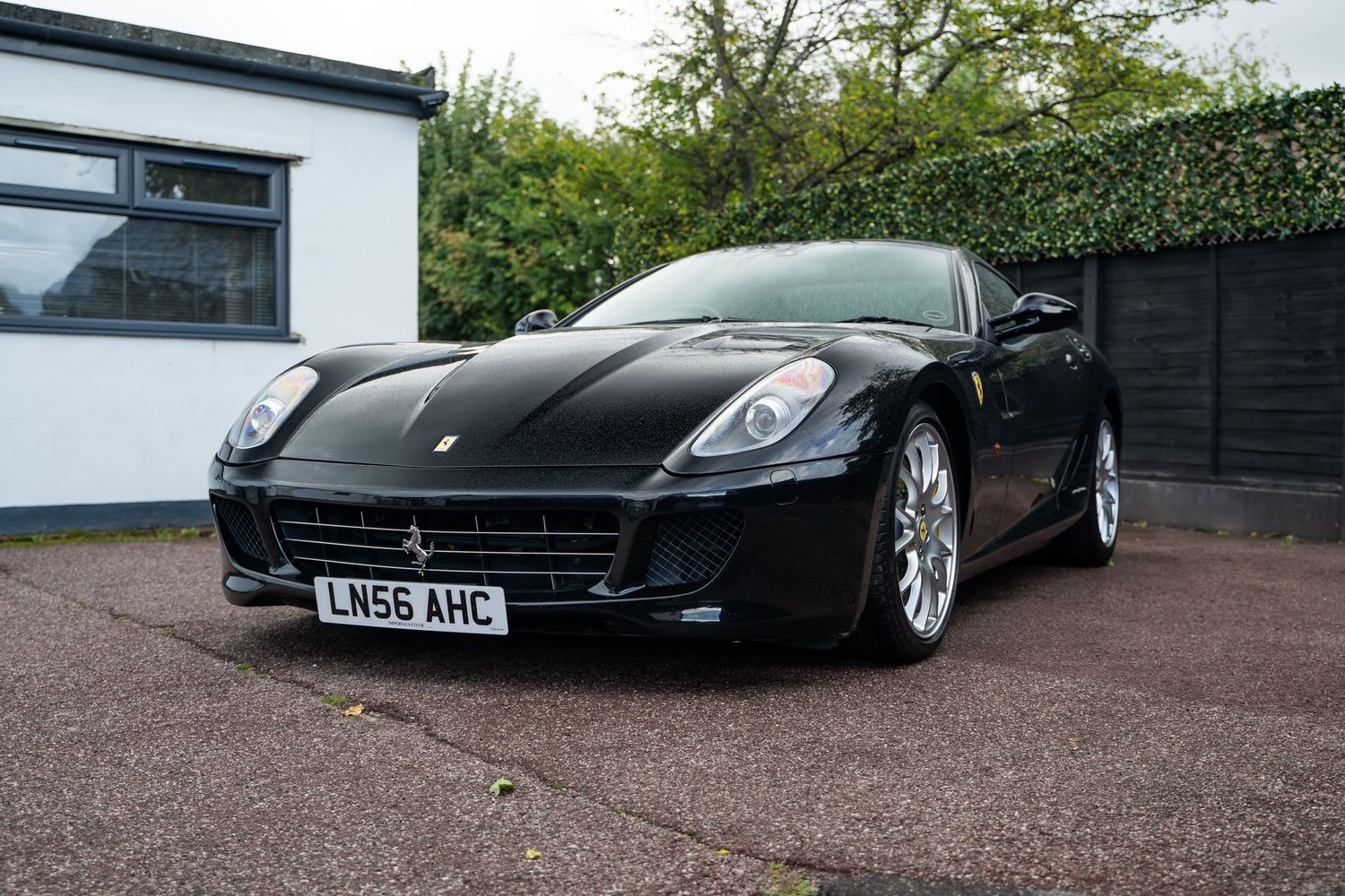 Black Ferrari 599 GTB sports car parked on driveway with British license plate.