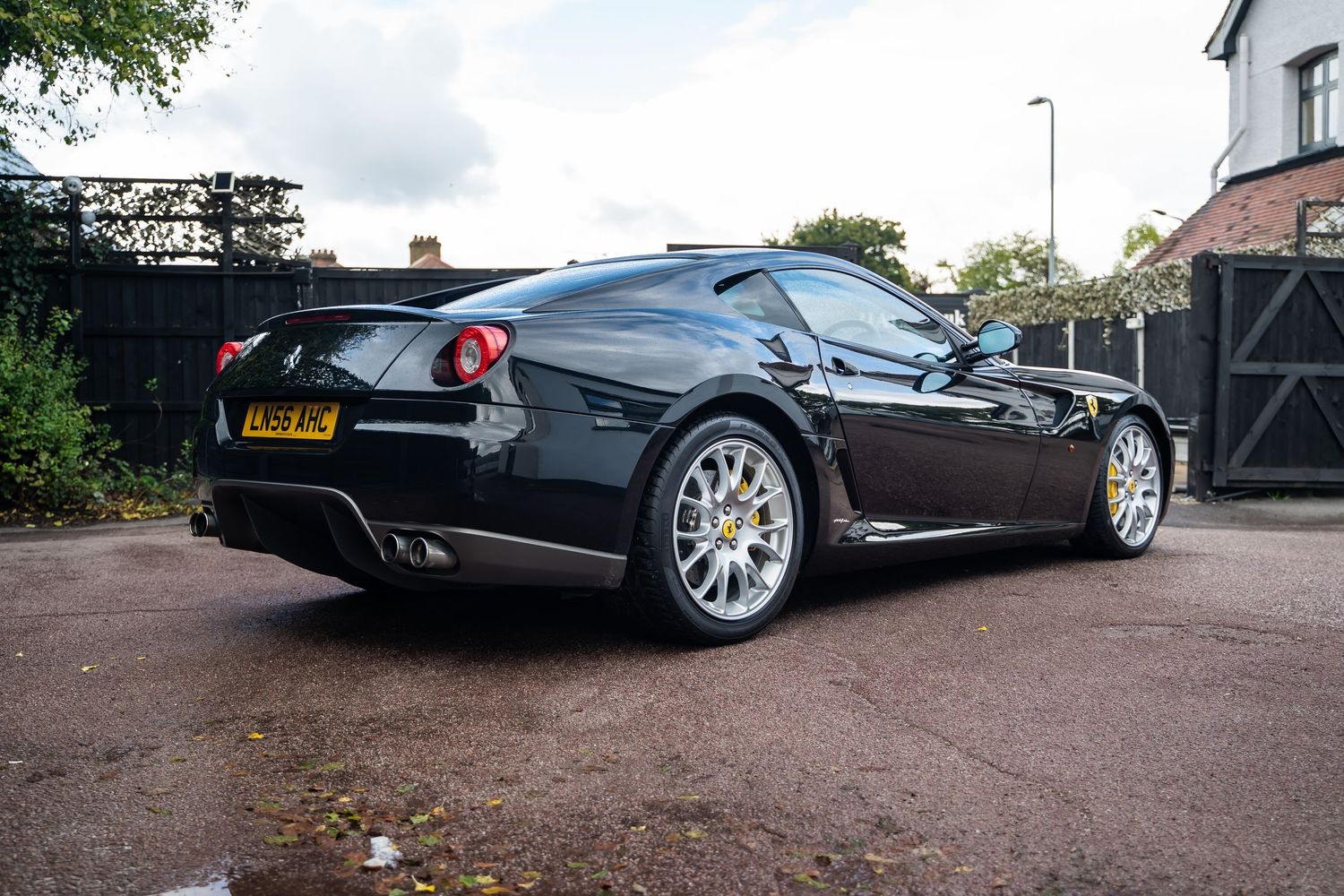 Black Ferrari sports car parked on gravel driveway with trees in background.
