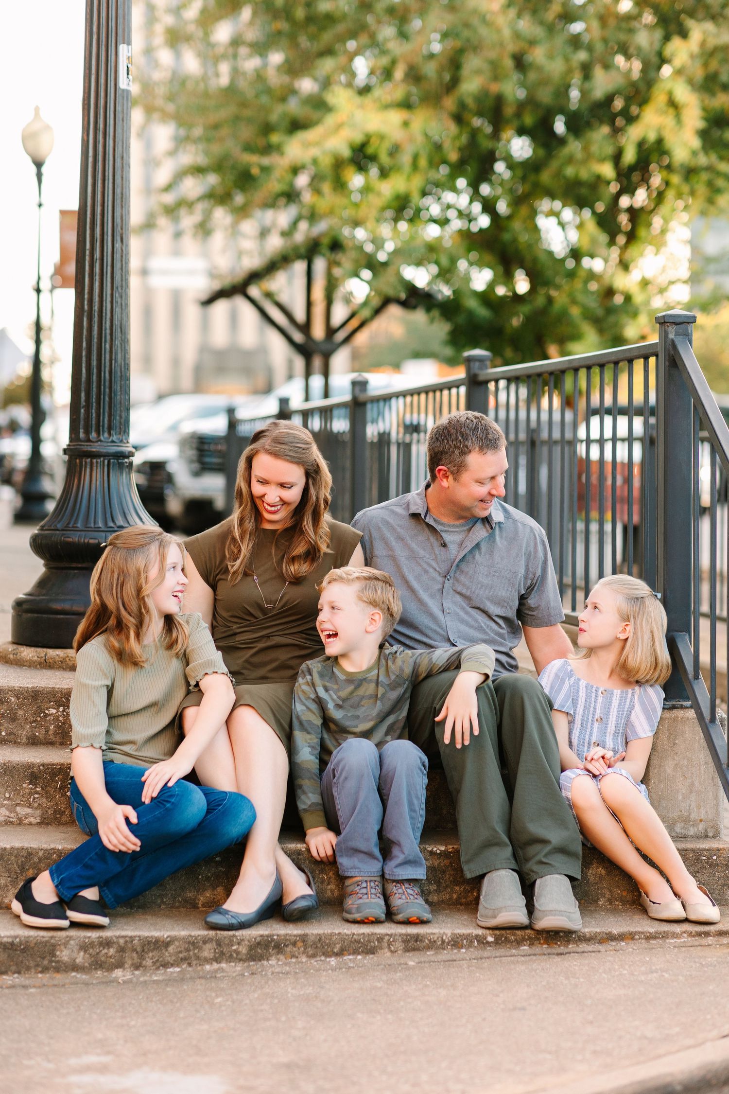 Relaxed family sitting together on stone steps outdoors under trees on a sunny afternoon.
