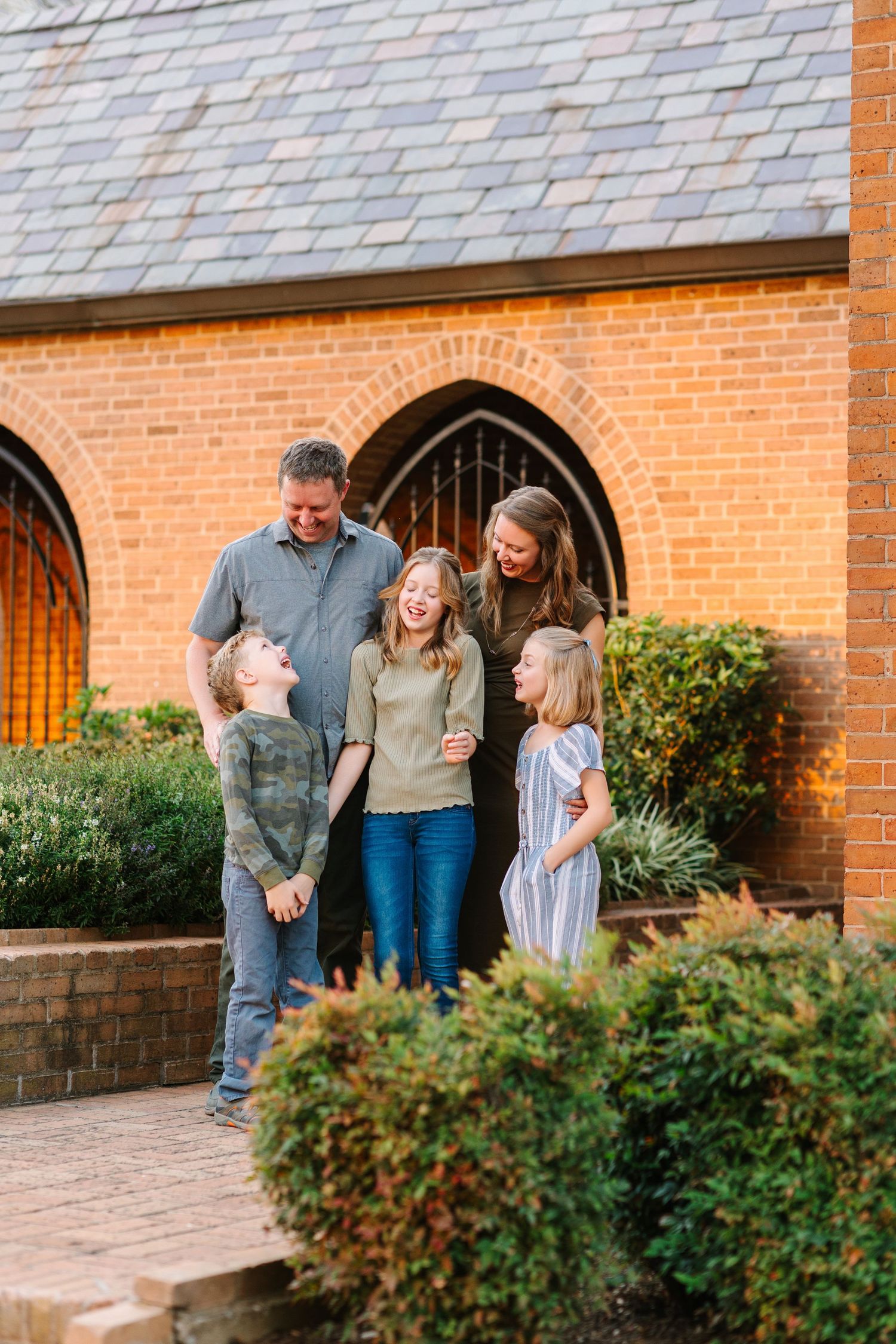 Family enjoying a playful moment together on a brick patio outside a church building with arched doorways.
