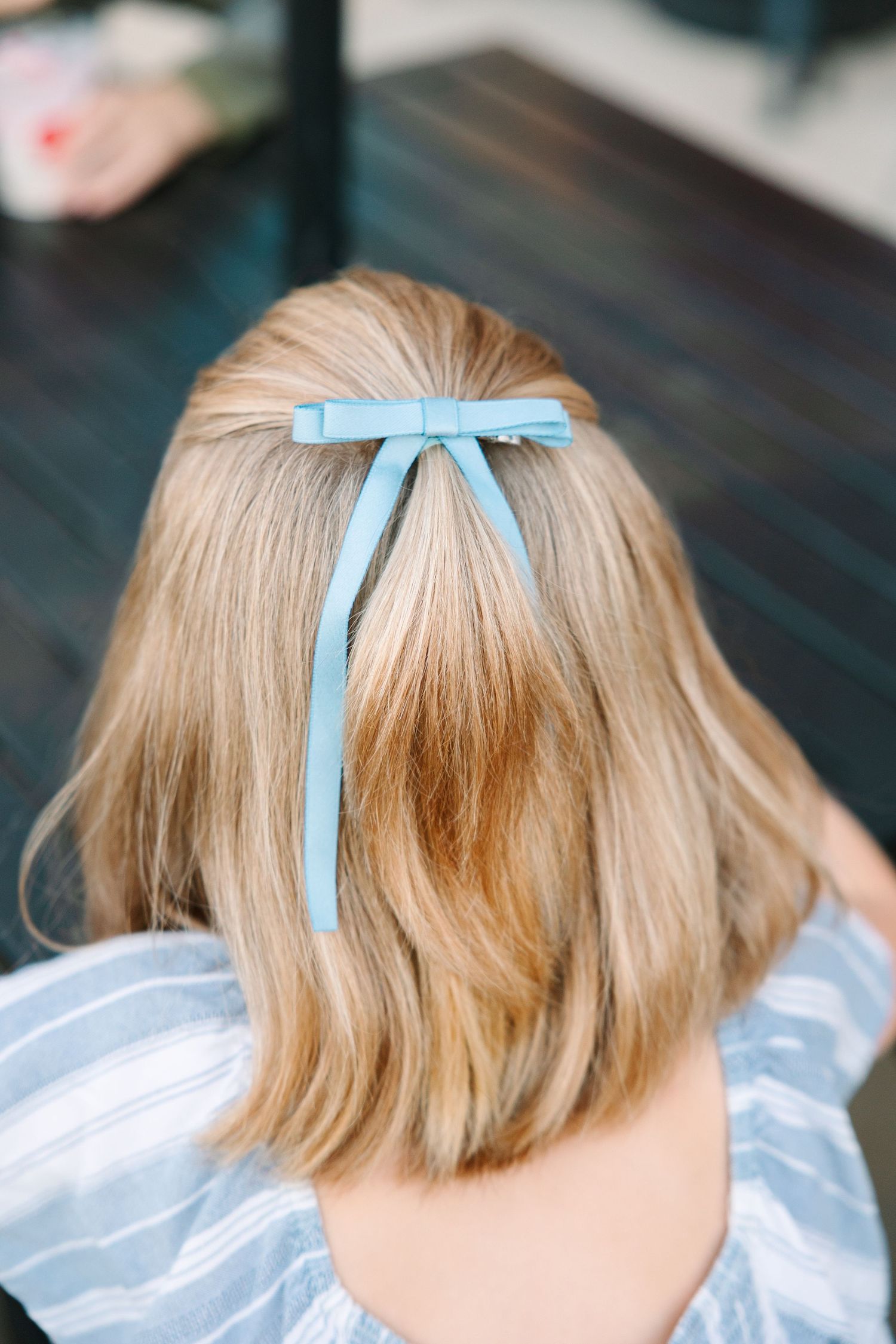 Light blue ribbon bow decorates blonde hair styled in a short blunt cut from behind.