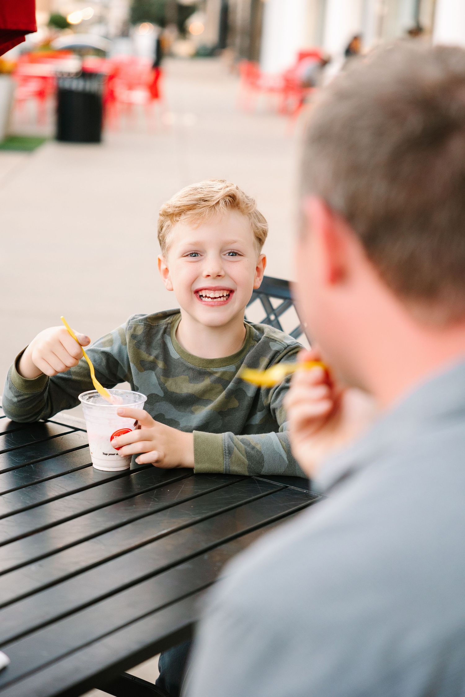 Happy child eating ice cream while sitting at black patio table outdoors.