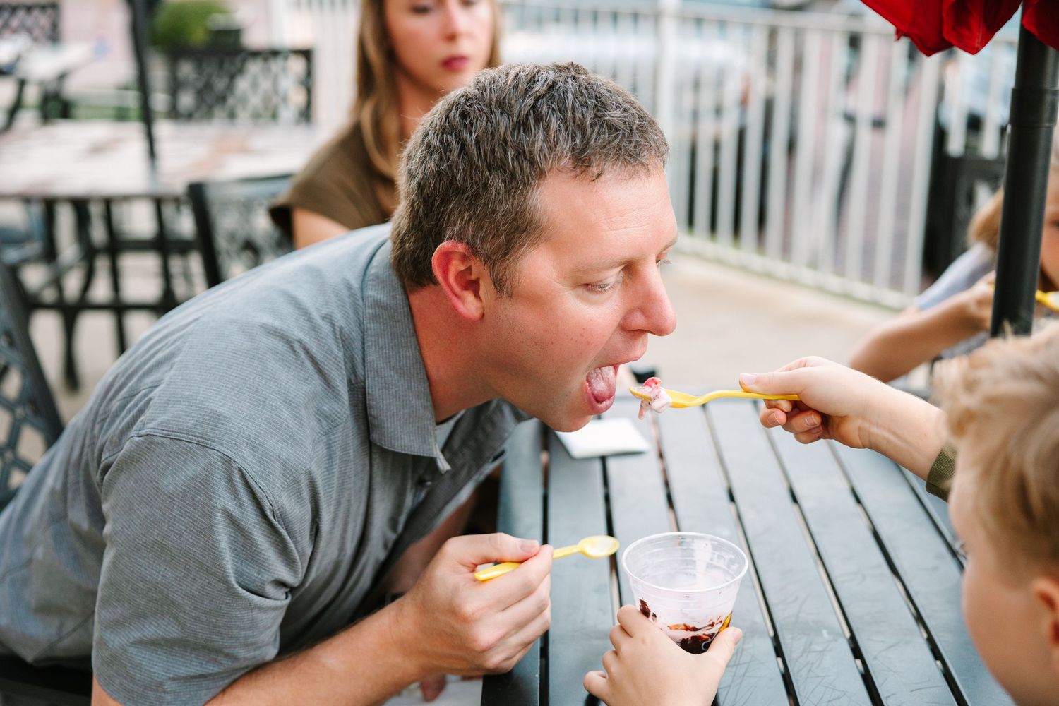Family enjoying ice cream treats together at an outdoor patio table on a sunny day.