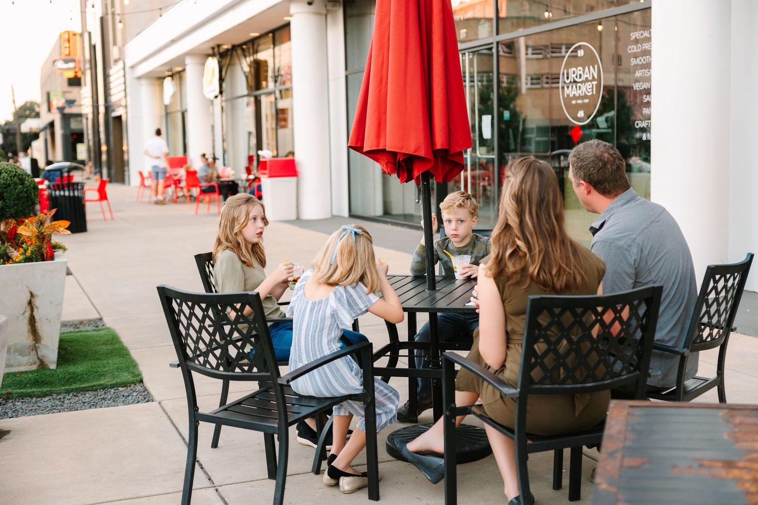 People gathered at outdoor restaurant tables under red umbrellas on a summer afternoon.